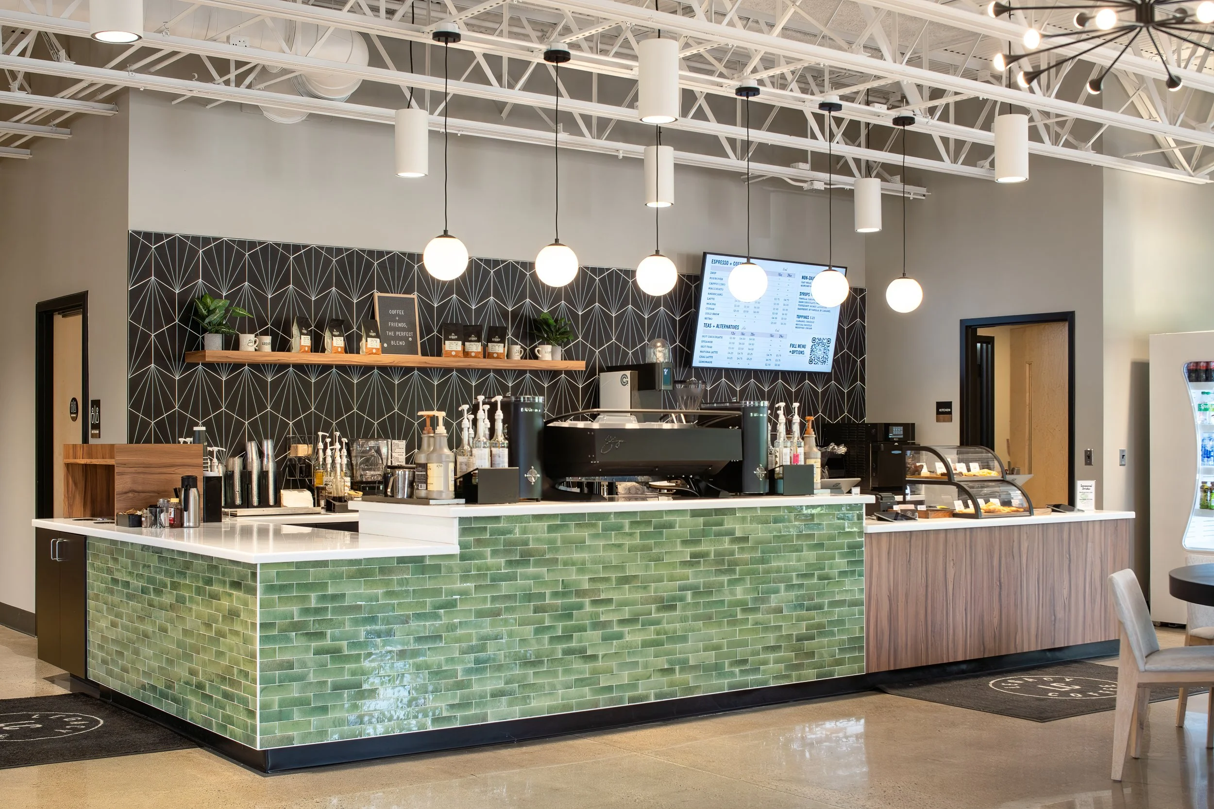 Coffee bar with green tiled counter, black geometric backsplash, and modern pendant lighting.