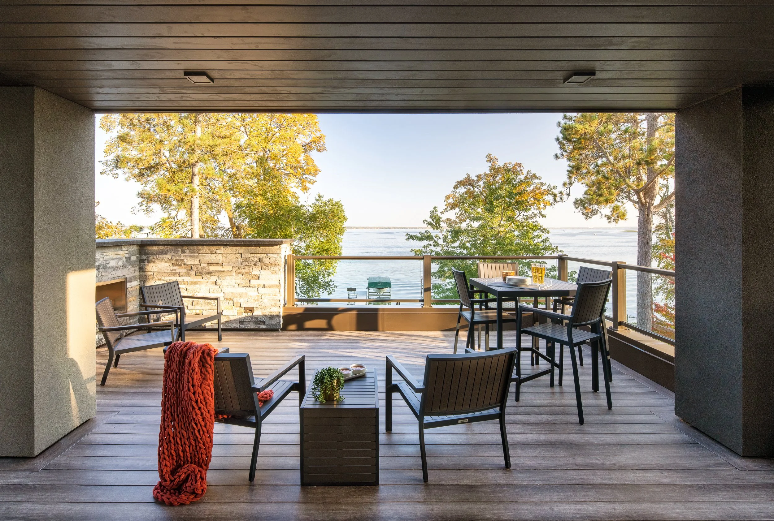 Covered outdoor terrace with seating, dining area, and lake views framed by autumn trees.