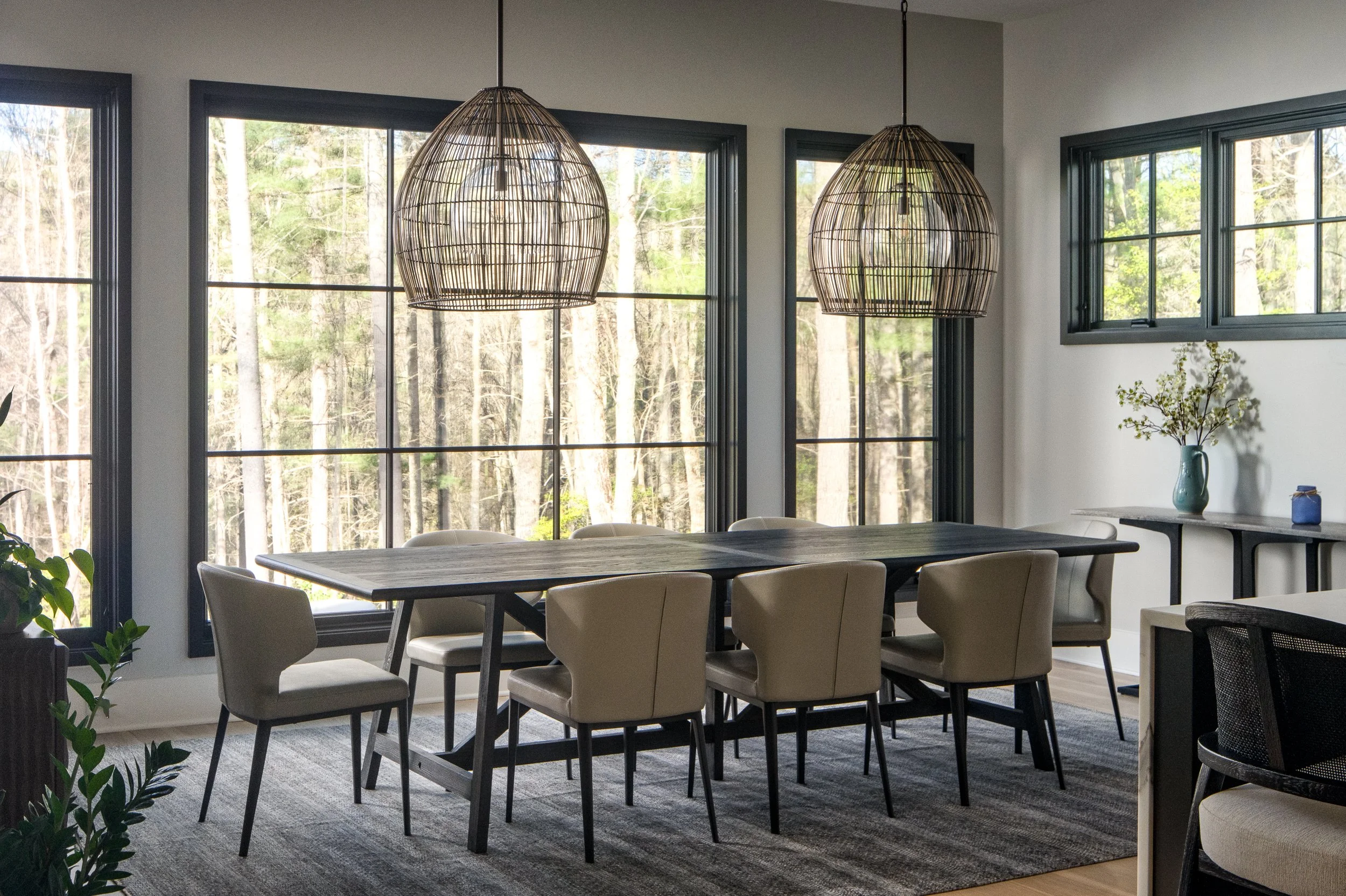 Dining room with wicker pendant lights and large black-framed windows.