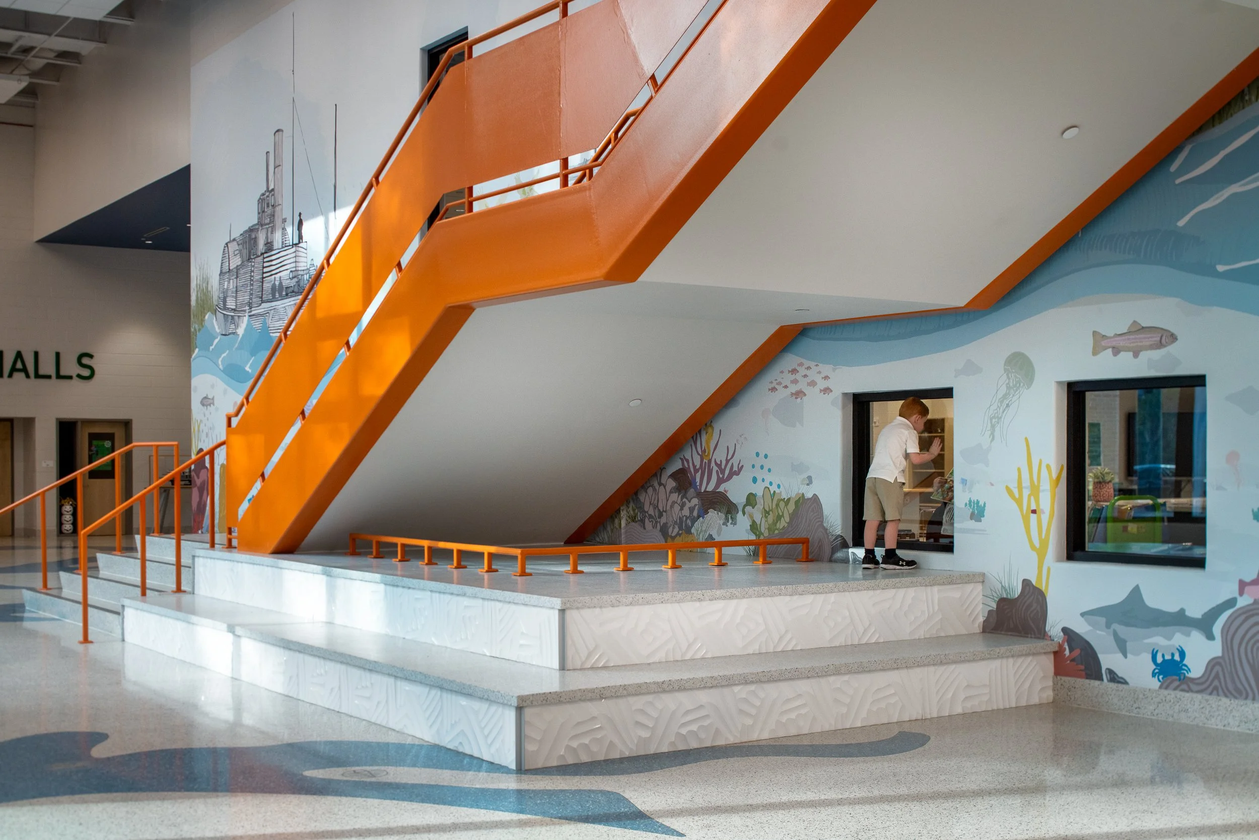 Indoor water-themed play area with an orange stairway, mural depicting underwater scene, and a young boy playing.