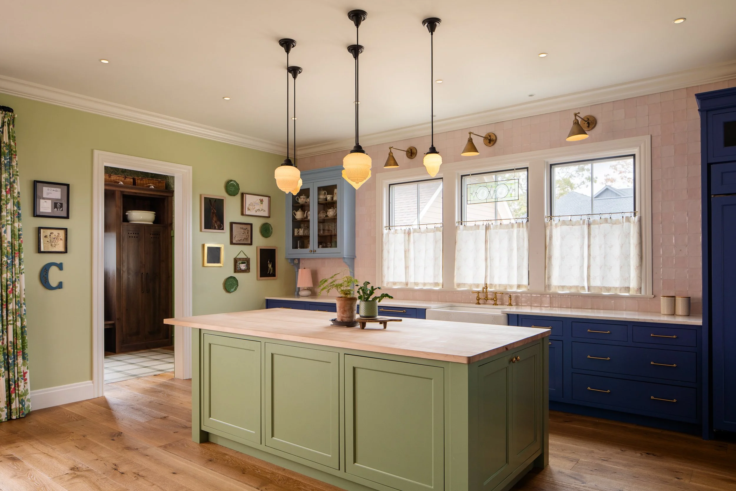 Colorful kitchen featuring a green island, blue cabinetry, pink tile, and black pendant lights