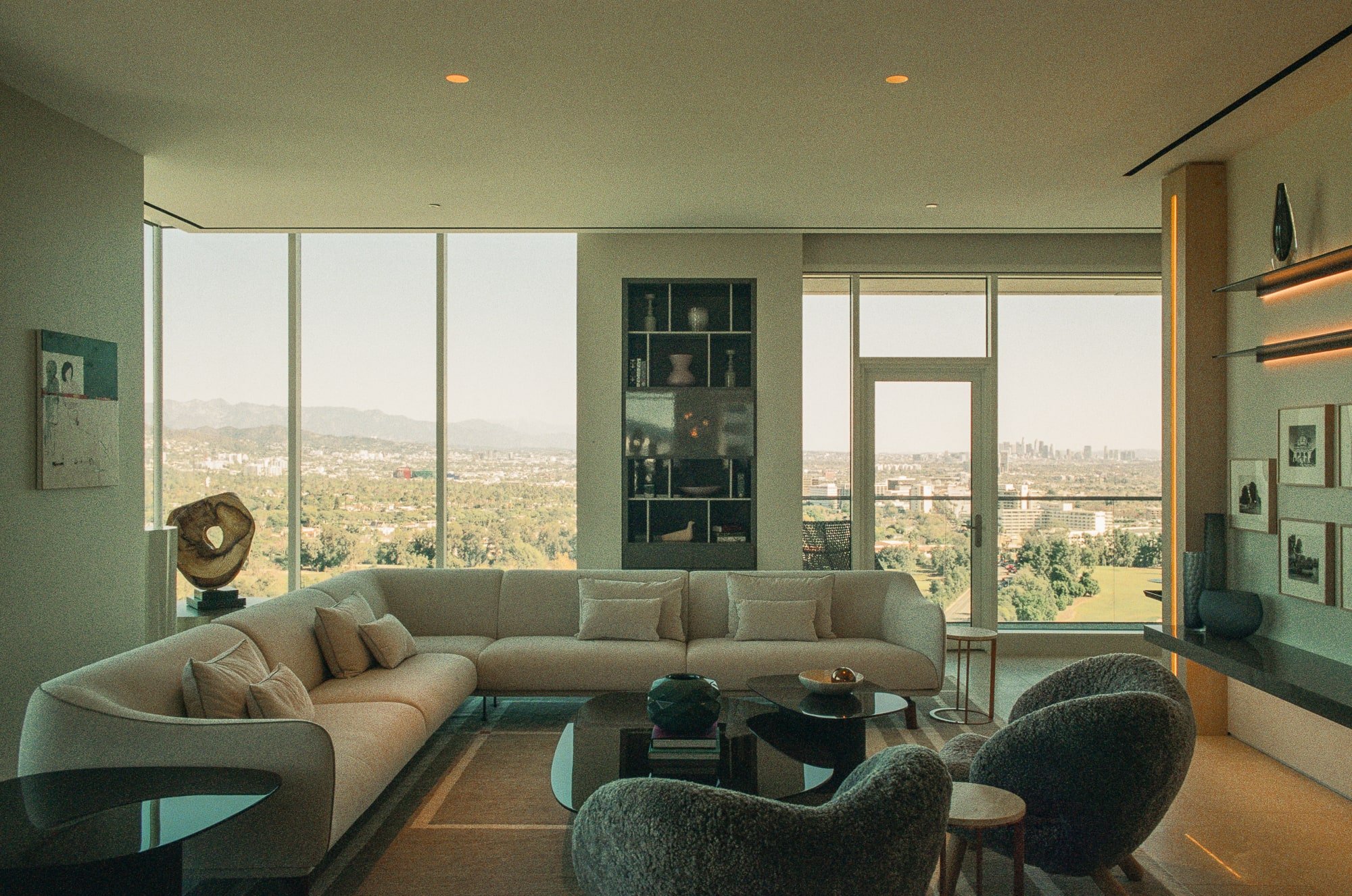 Contemporary living room with curved sectional seating, textured lounge chairs, and floor-to-ceiling windows overlooking Los Angeles.