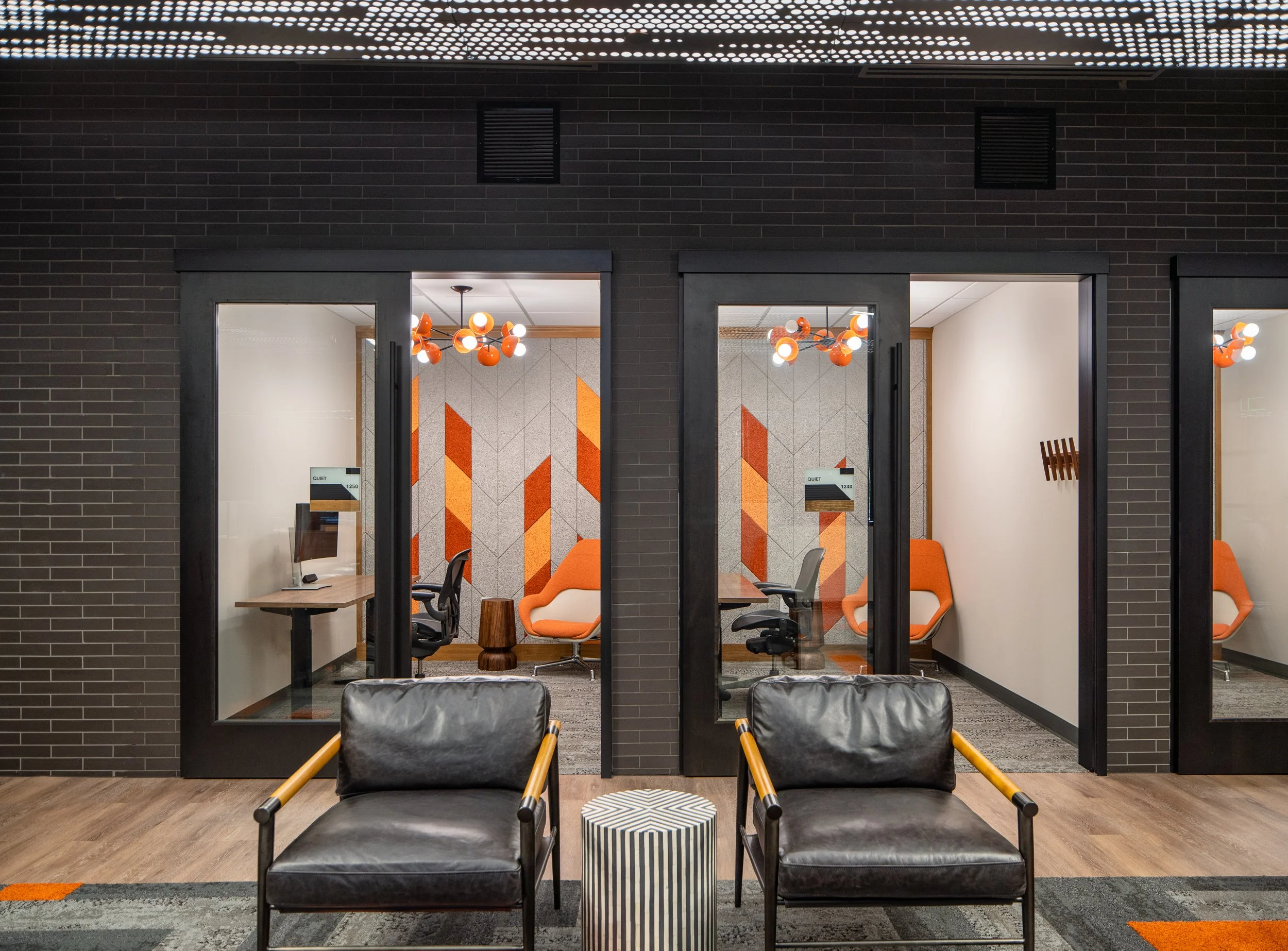 Private meeting rooms with glass walls, orange-accented lighting, and geometric wall panels.