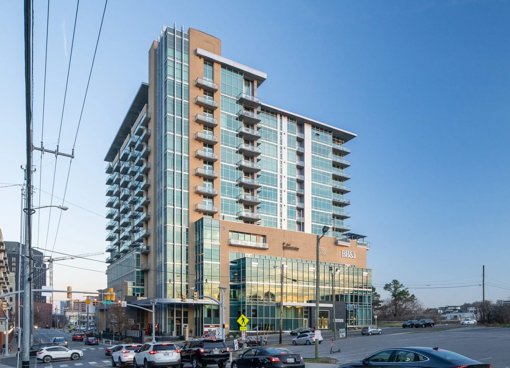 Mixed-use building in The Gulch Nashville with glass and stone facade, ground floor retail including HOSA signage, street level activity, and blue sky