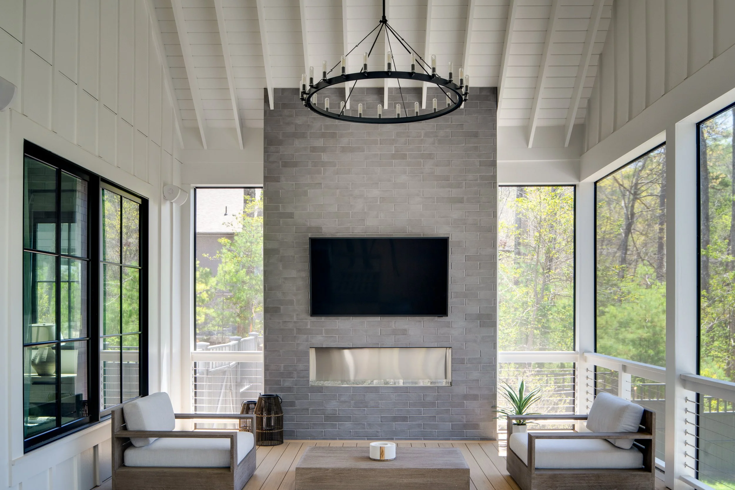 Screened porch with a fireplace, chandelier, and outdoor seating.