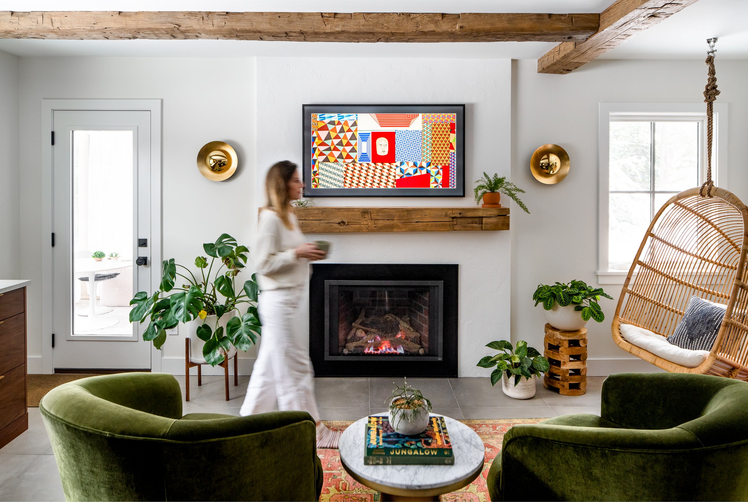 Cozy living room with a stone fireplace, green velvet chairs, rustic wood accents, and warm ambient light