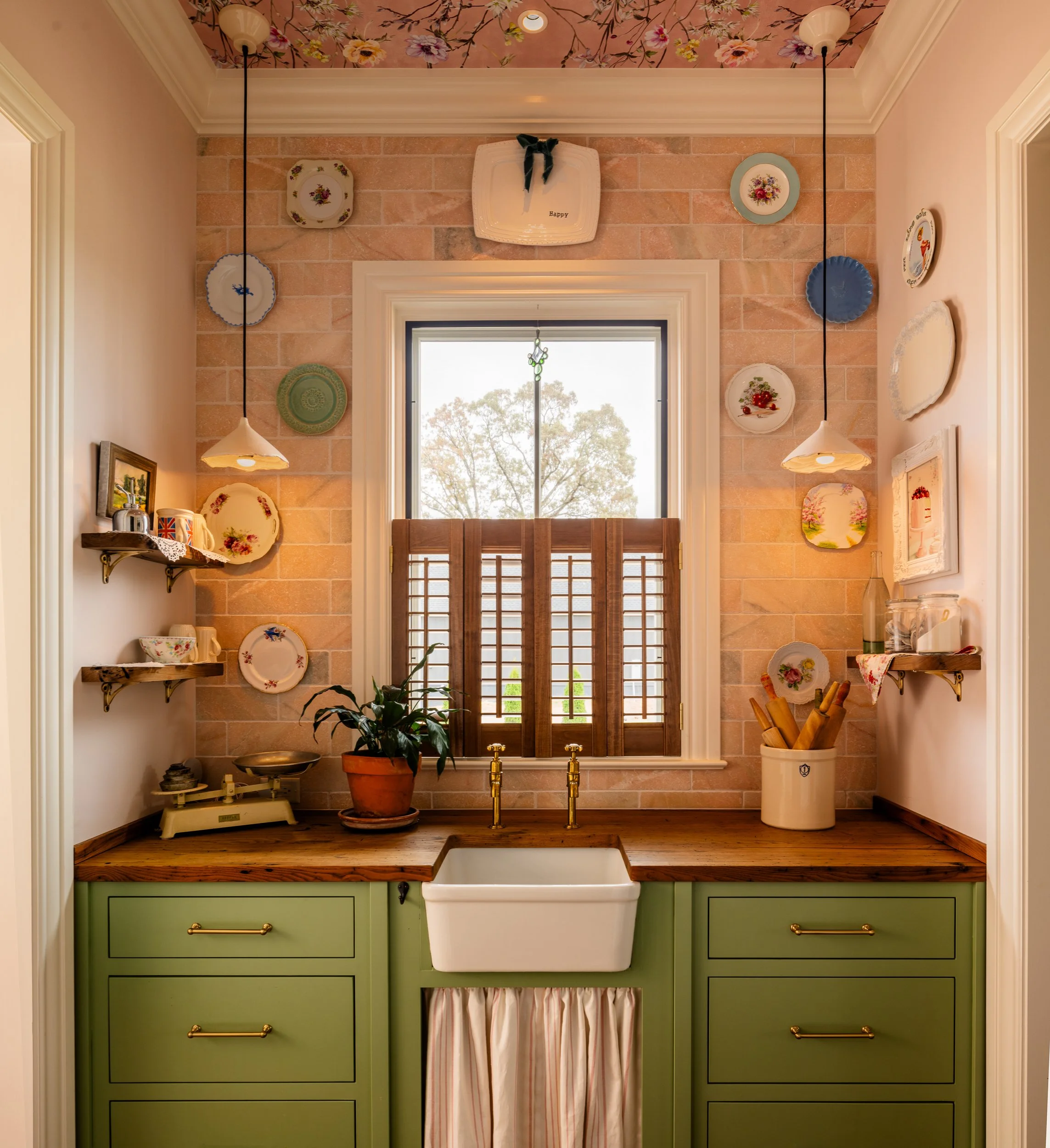 Scullery with farmhouse sink, wood countertop, green drawers, and decorative plates
