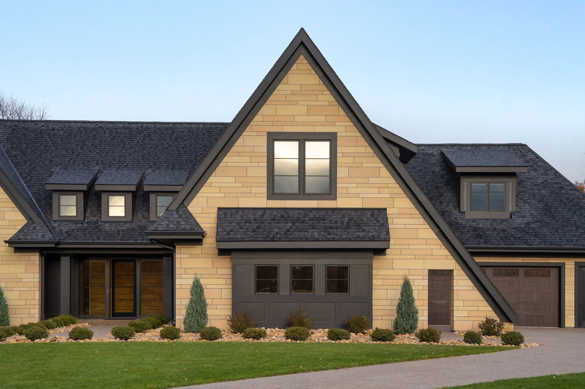 Close-up view of a modern home's front entrance with stone siding, black trim, and dormer windows.