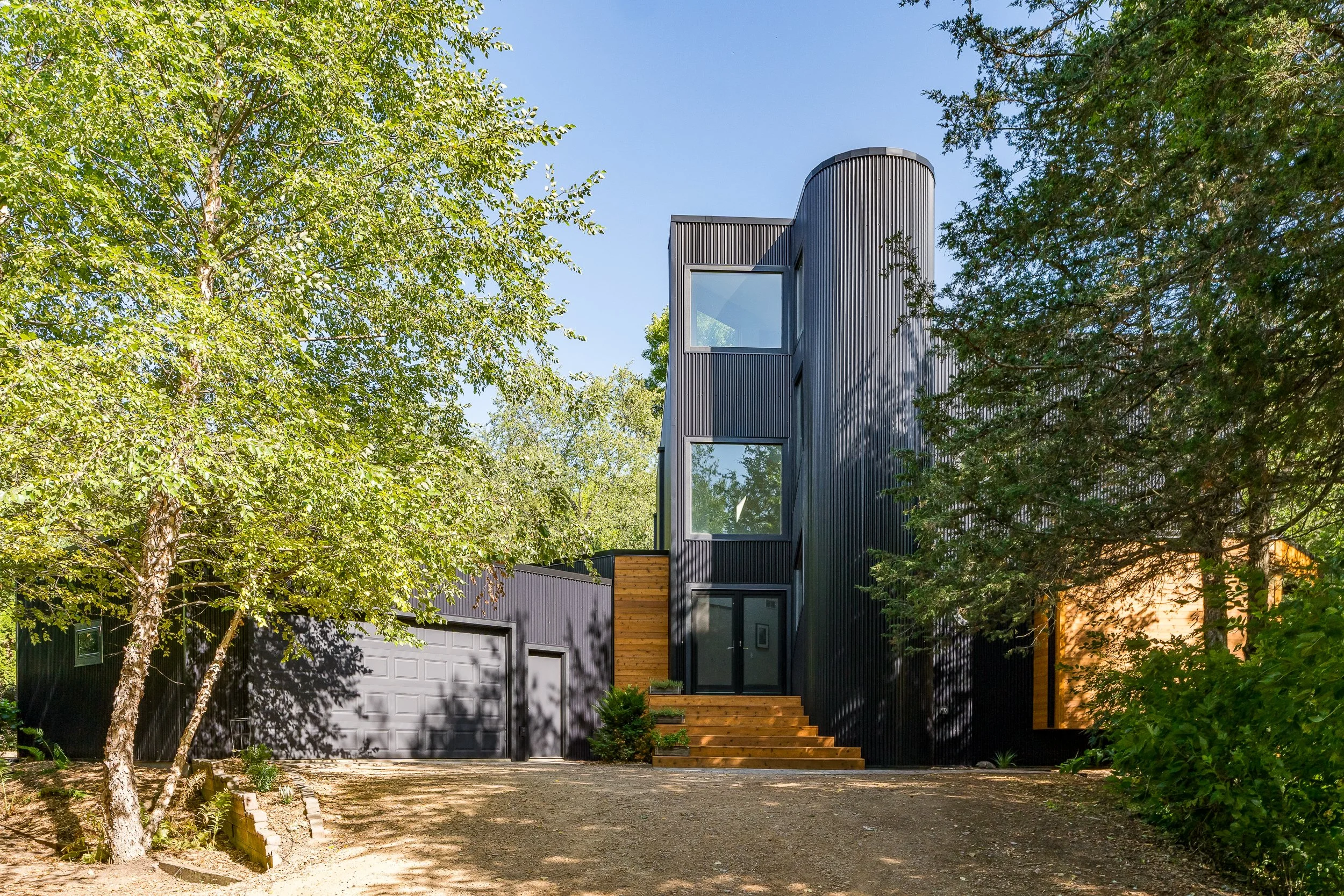 Contemporary black wood home surrounded by lush greenery.