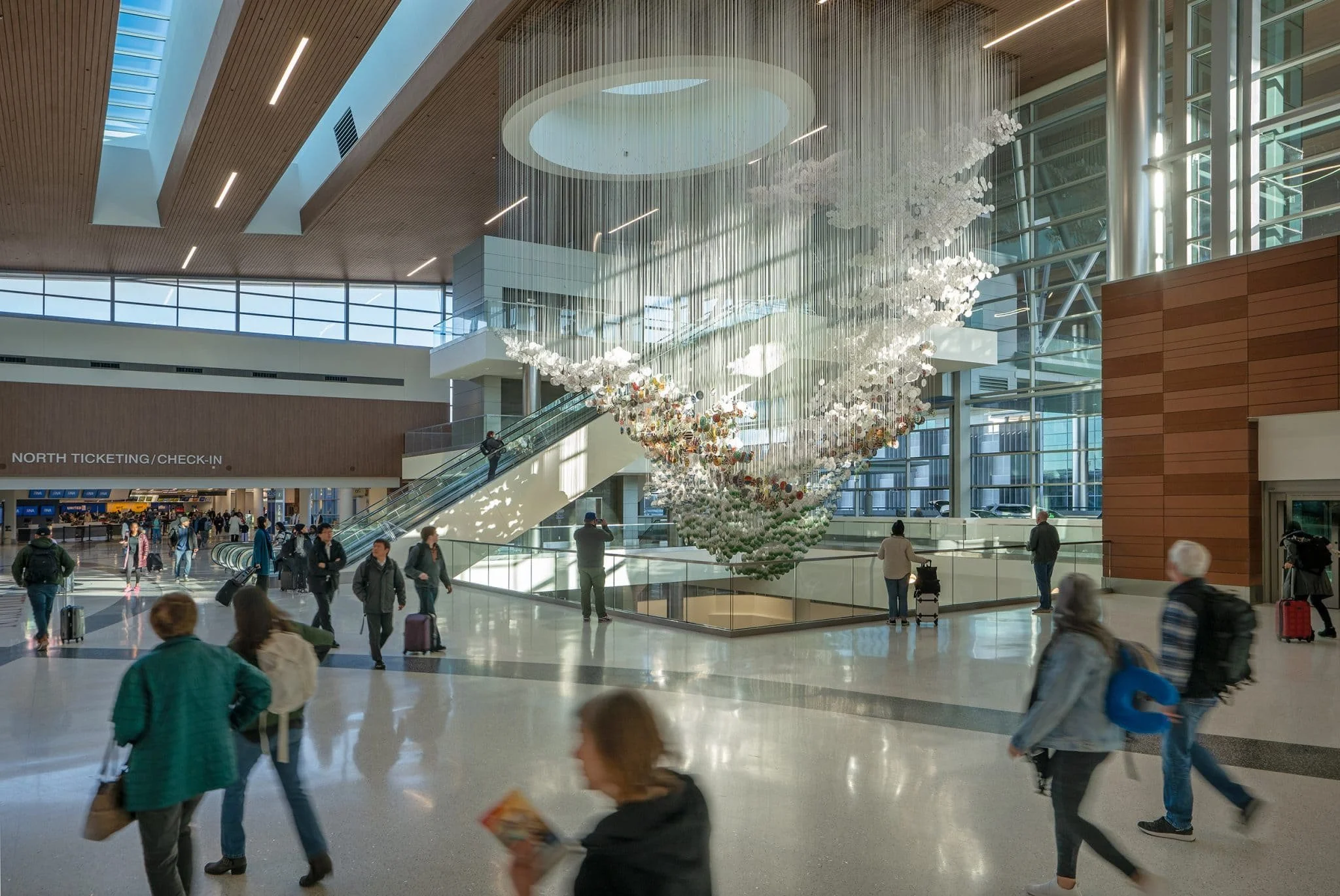 Passengers move through a spacious concourse beneath a layered installation of white strands and colorful circular forms.