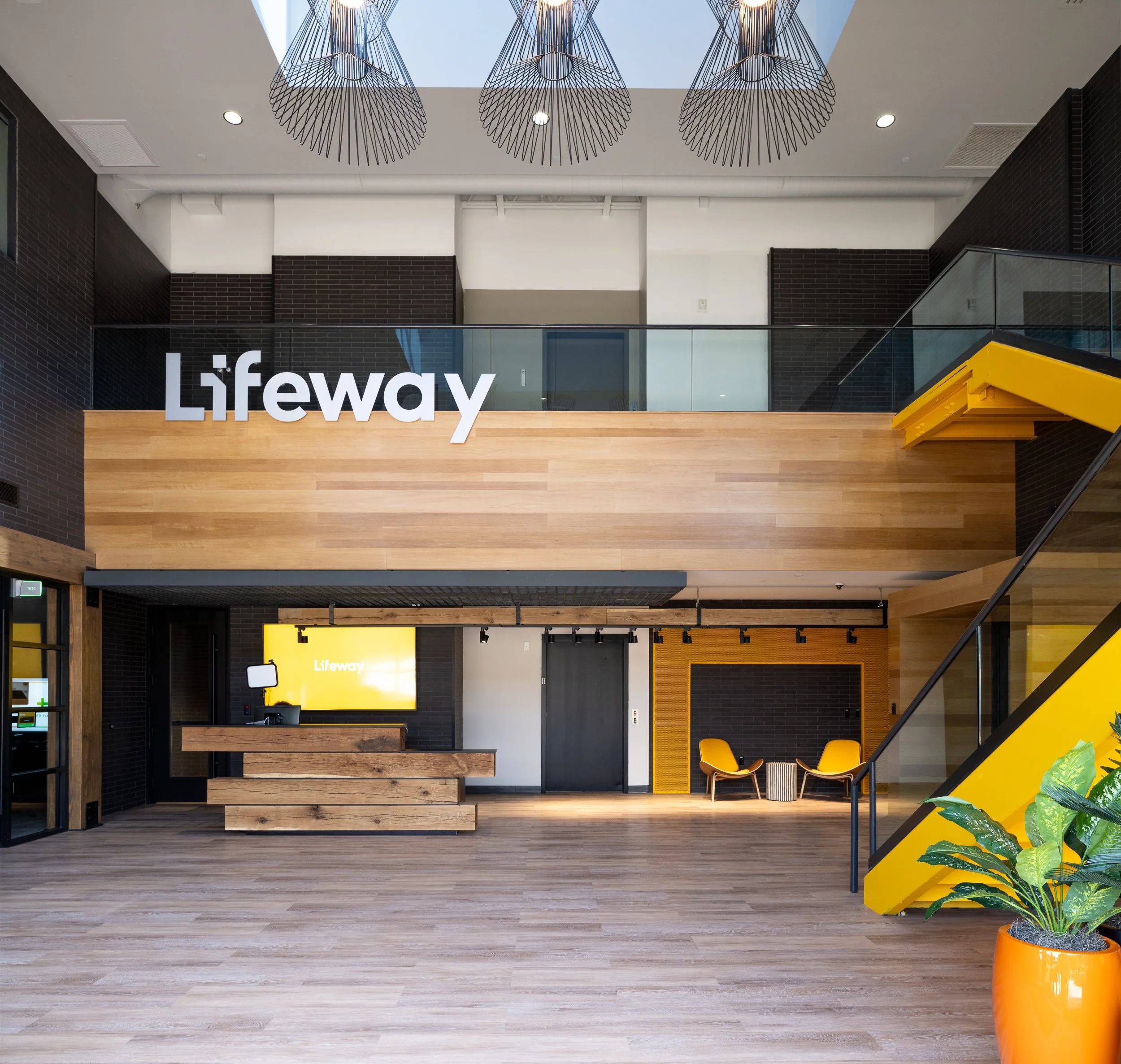 Spacious corporate lobby with wood finishes, a yellow staircase, and skylights.