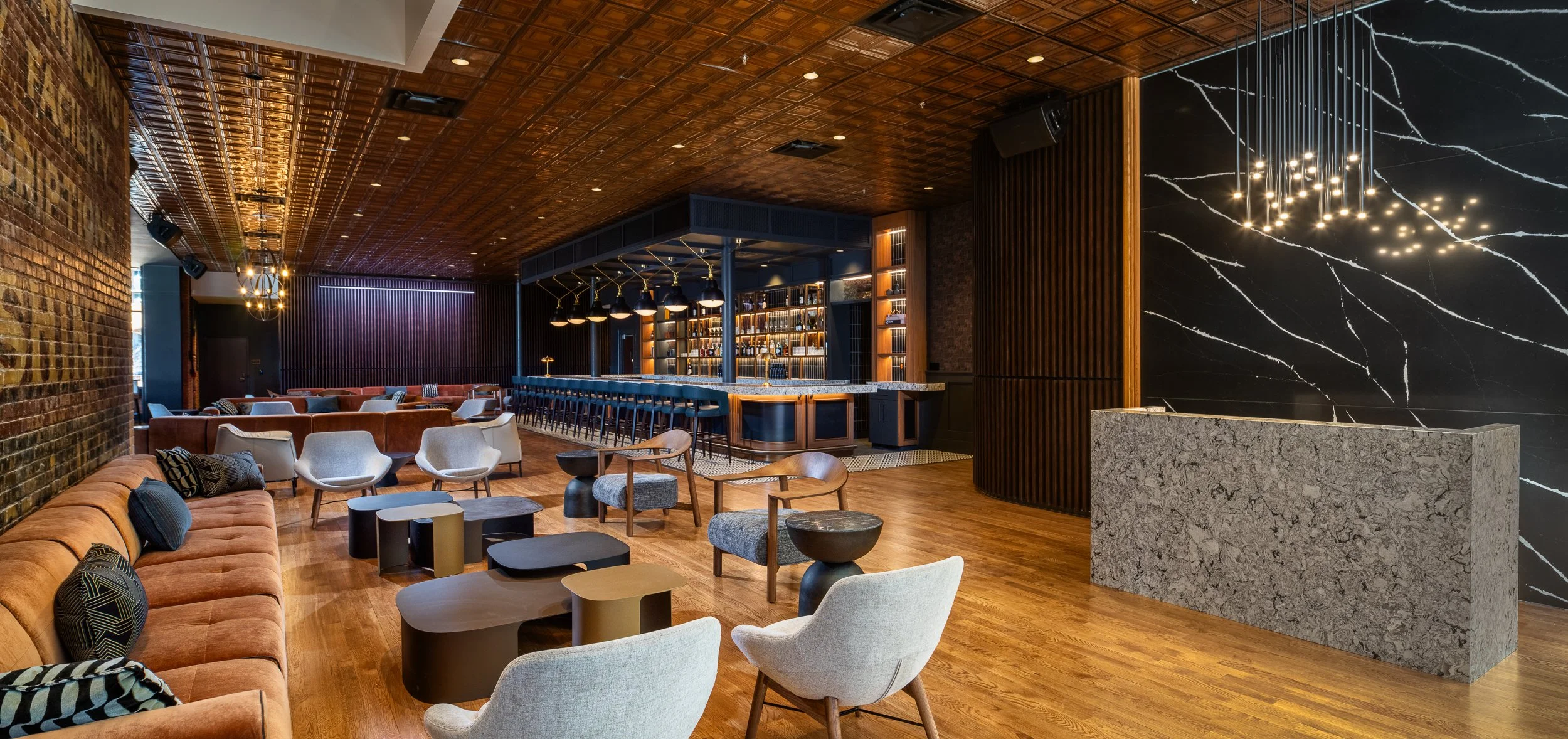 Lounge area with rust-colored velvet banquettes and a dramatic black-and-white veined stone feature wall on the right, looking toward the long brass-lit bar at the back of the room.