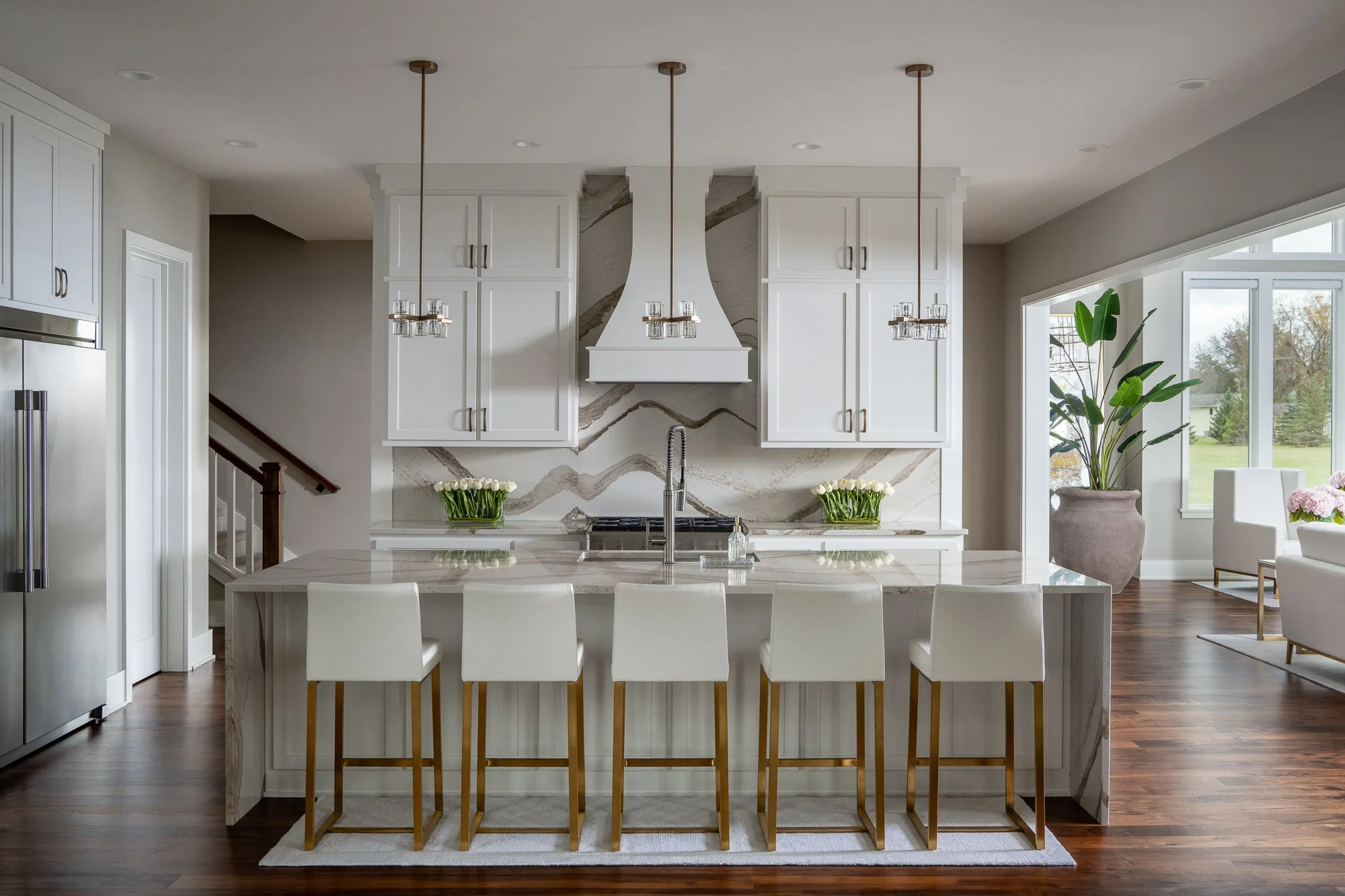 Luxury kitchen with a marble island, white cabinetry, and gold pendant lights.