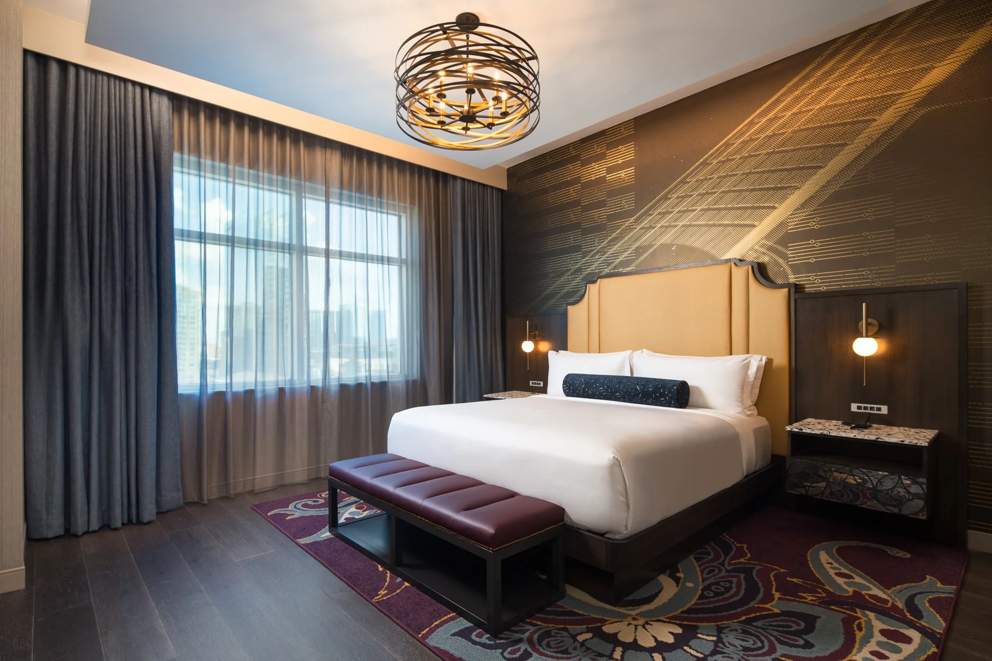 King bed in the Acoustic Suite with a gold upholstered headboard, dark wood furnishings, sheer drapery, and music-inspired feature wall.