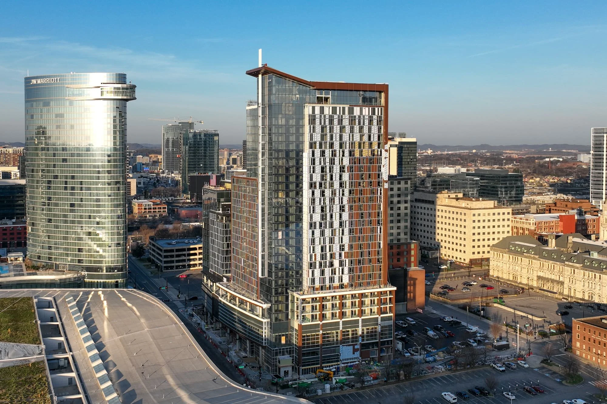 Aerial view of a tall glass building under construction near surrounding hotels, offices, and city streets in downtown Nashville.