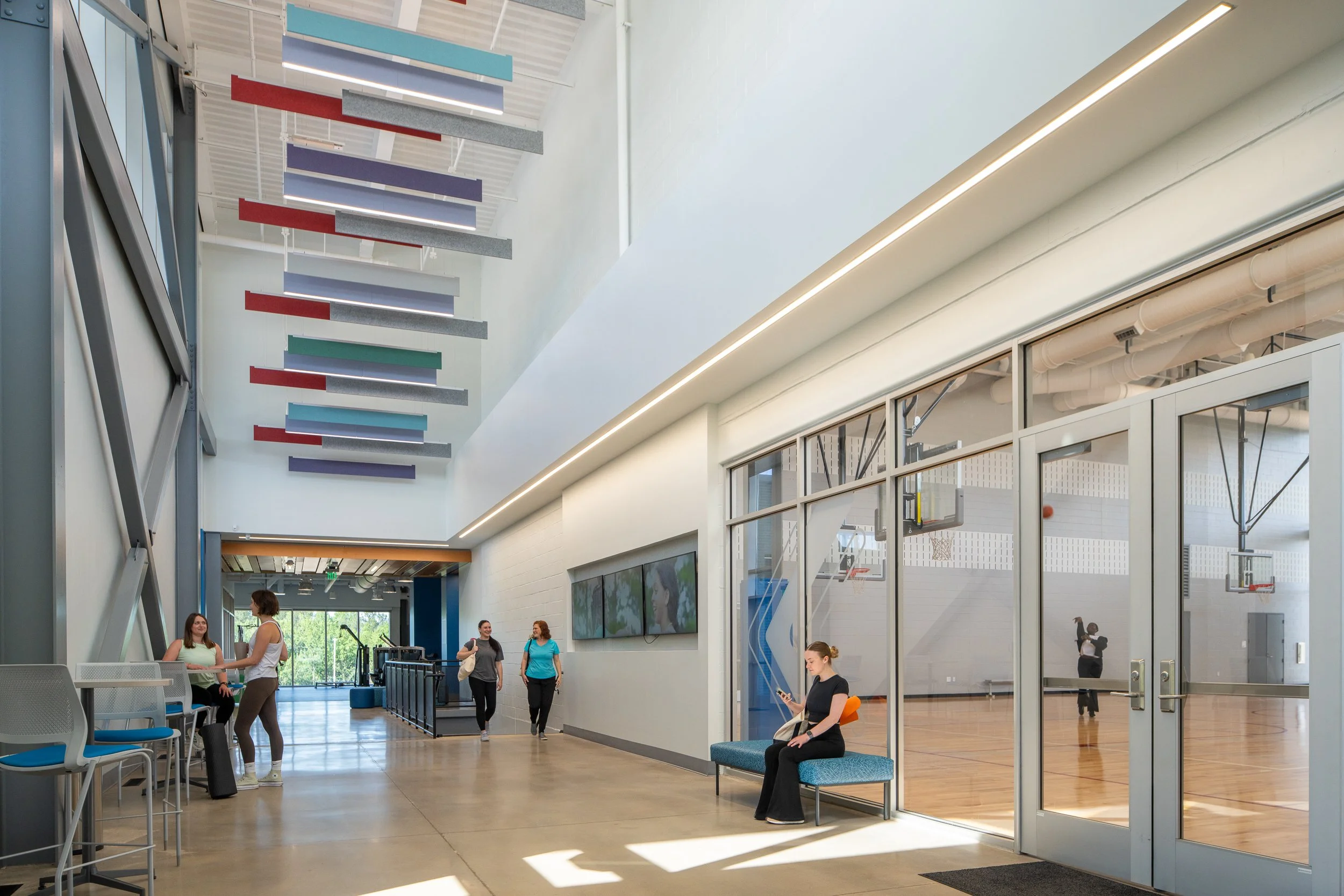 Bright seating area with suspended acoustic panels and glass doors opening to the indoor basketball courts.