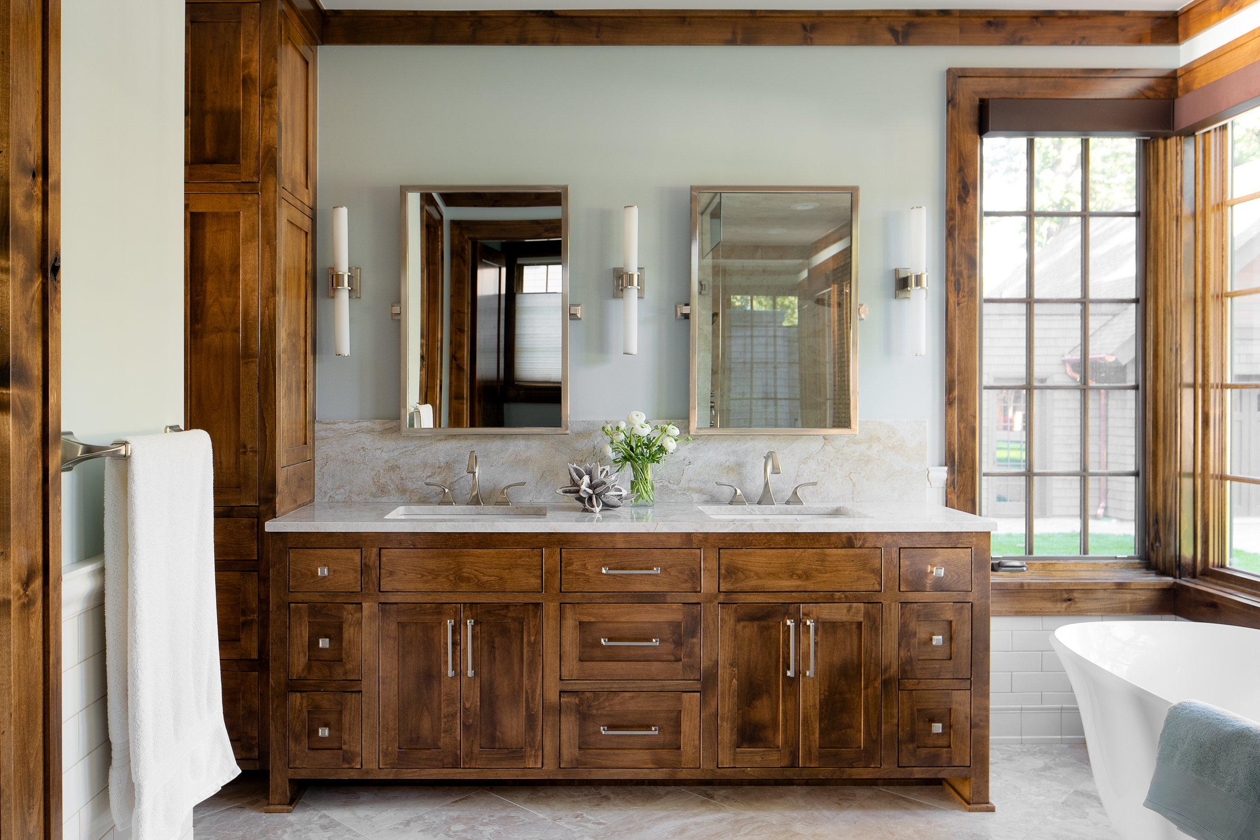 Bathroom with dual sinks and wood cabinetry near large window.