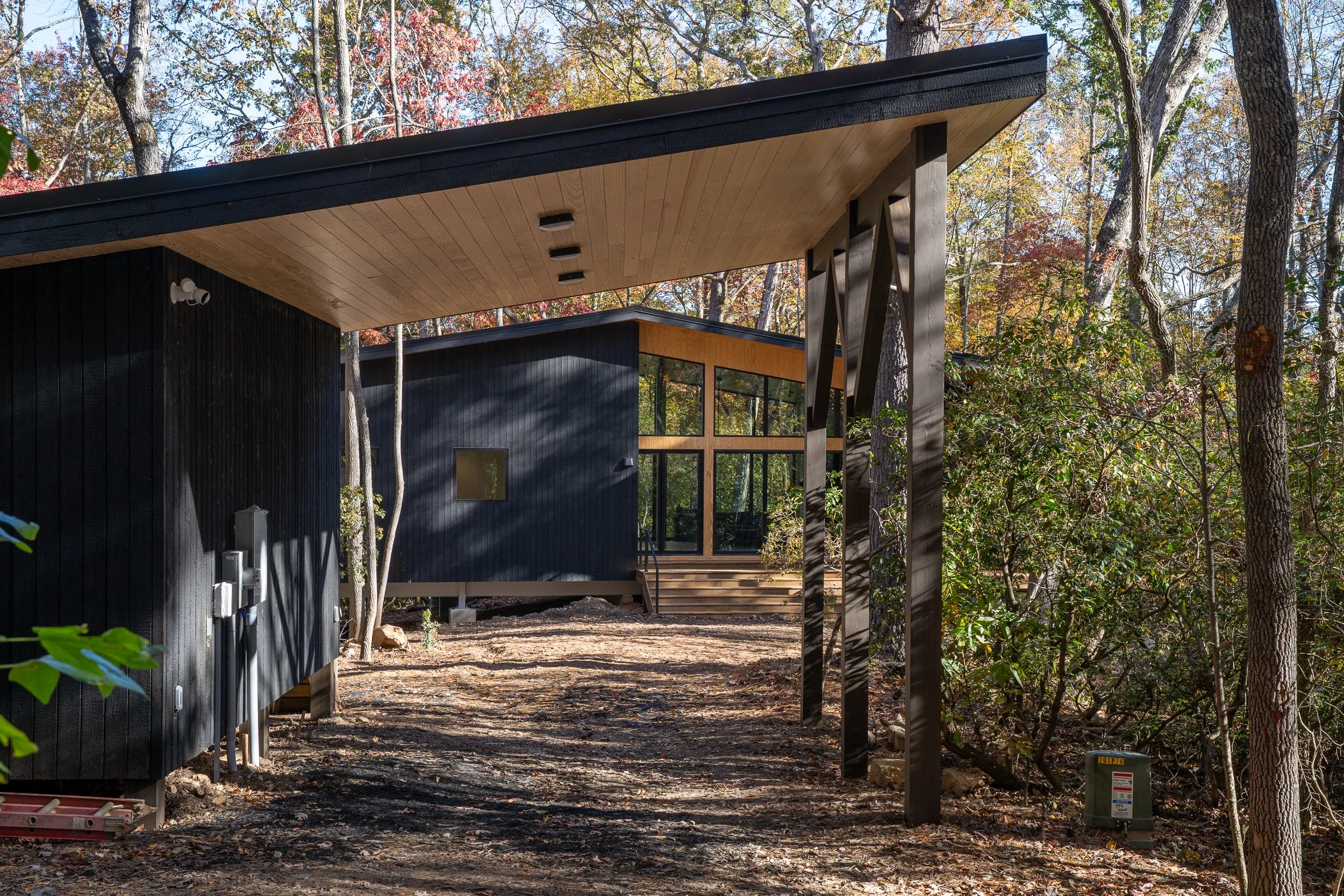 View beneath a deep roof overhang toward the burnt cedar home set back in the woods.