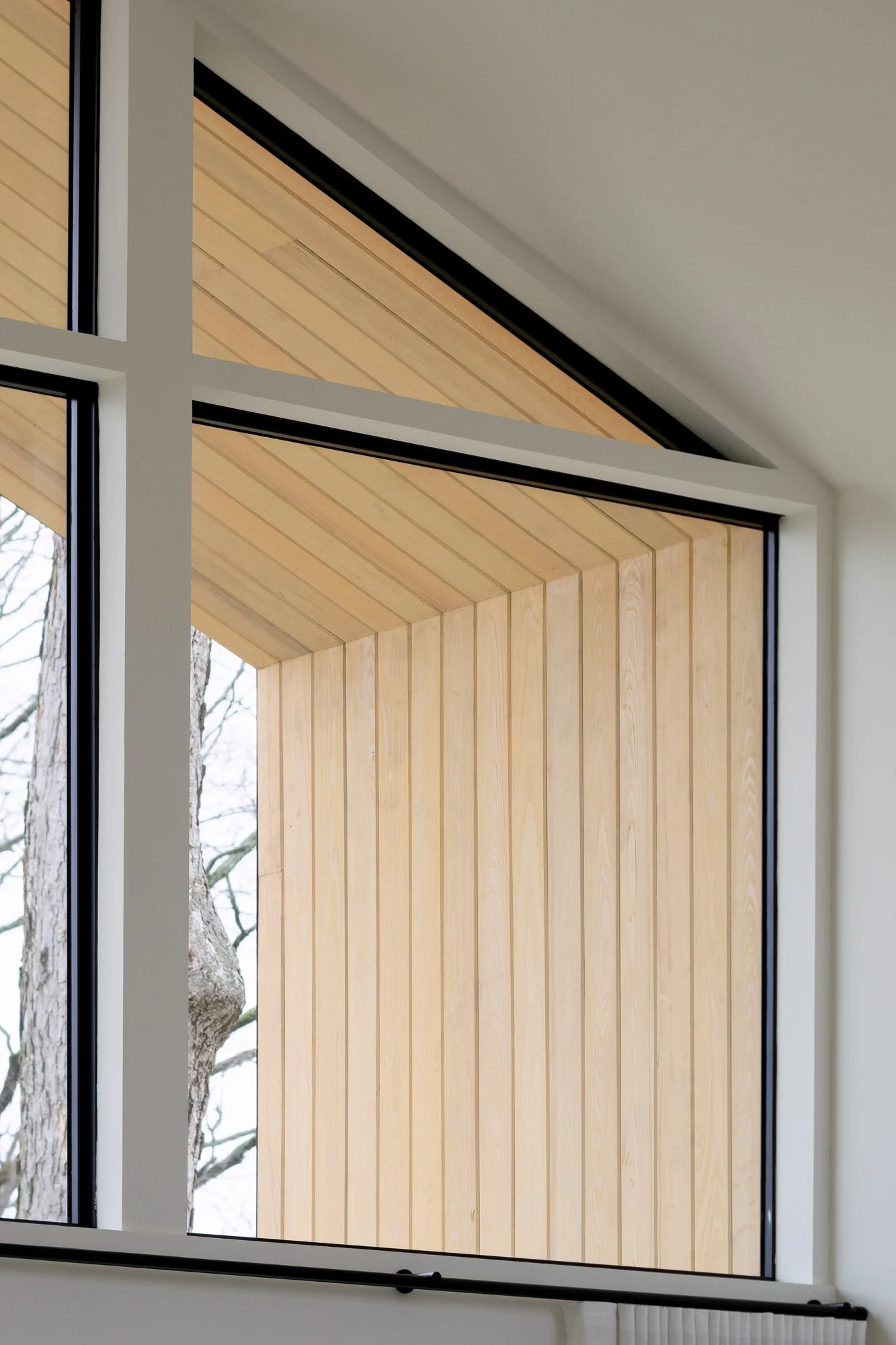 Close-up of gabled window corner with vertical wood cladding and black trim.