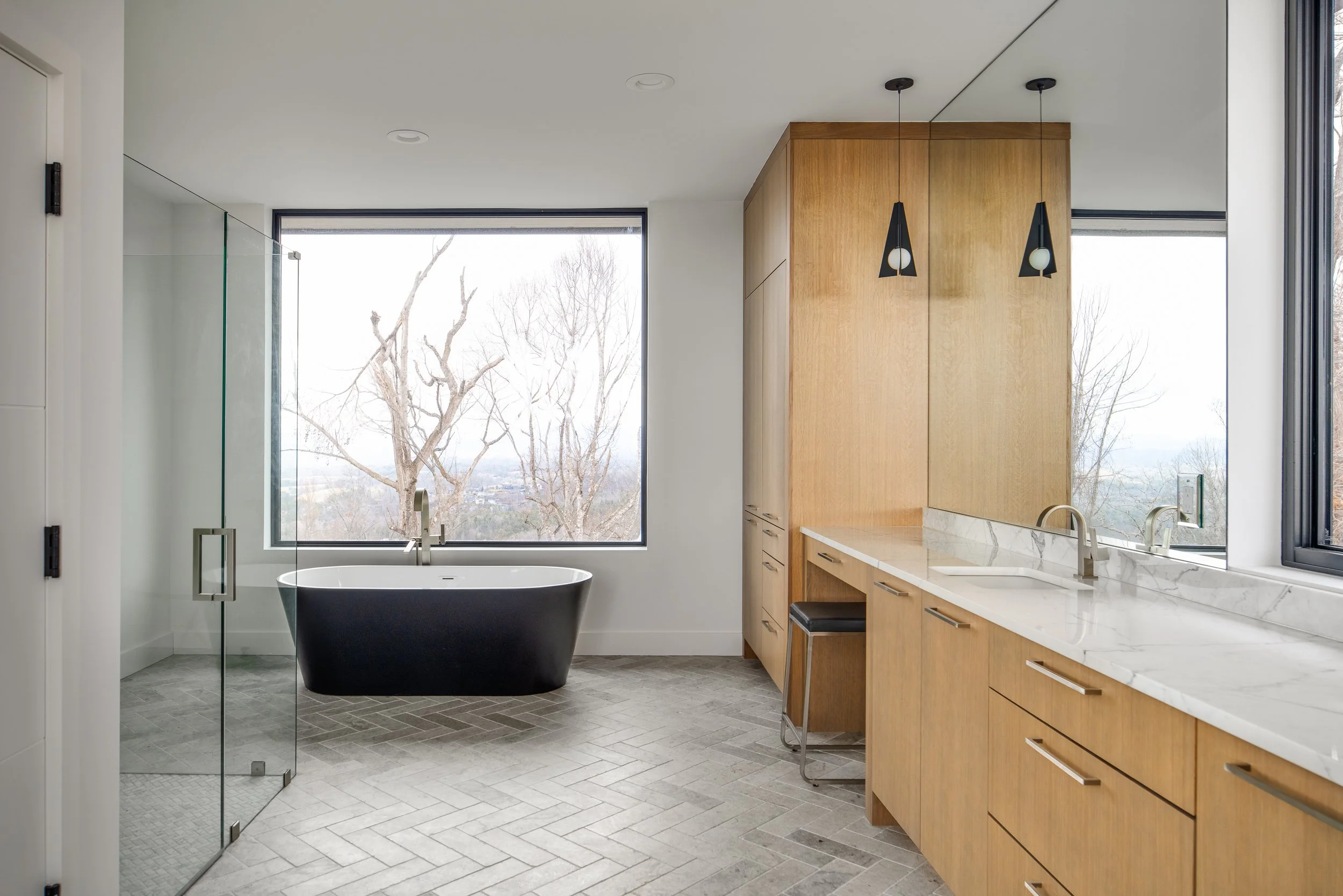 Primary bathroom with a freestanding black tub, glass shower, wood cabinetry, and mountain views.