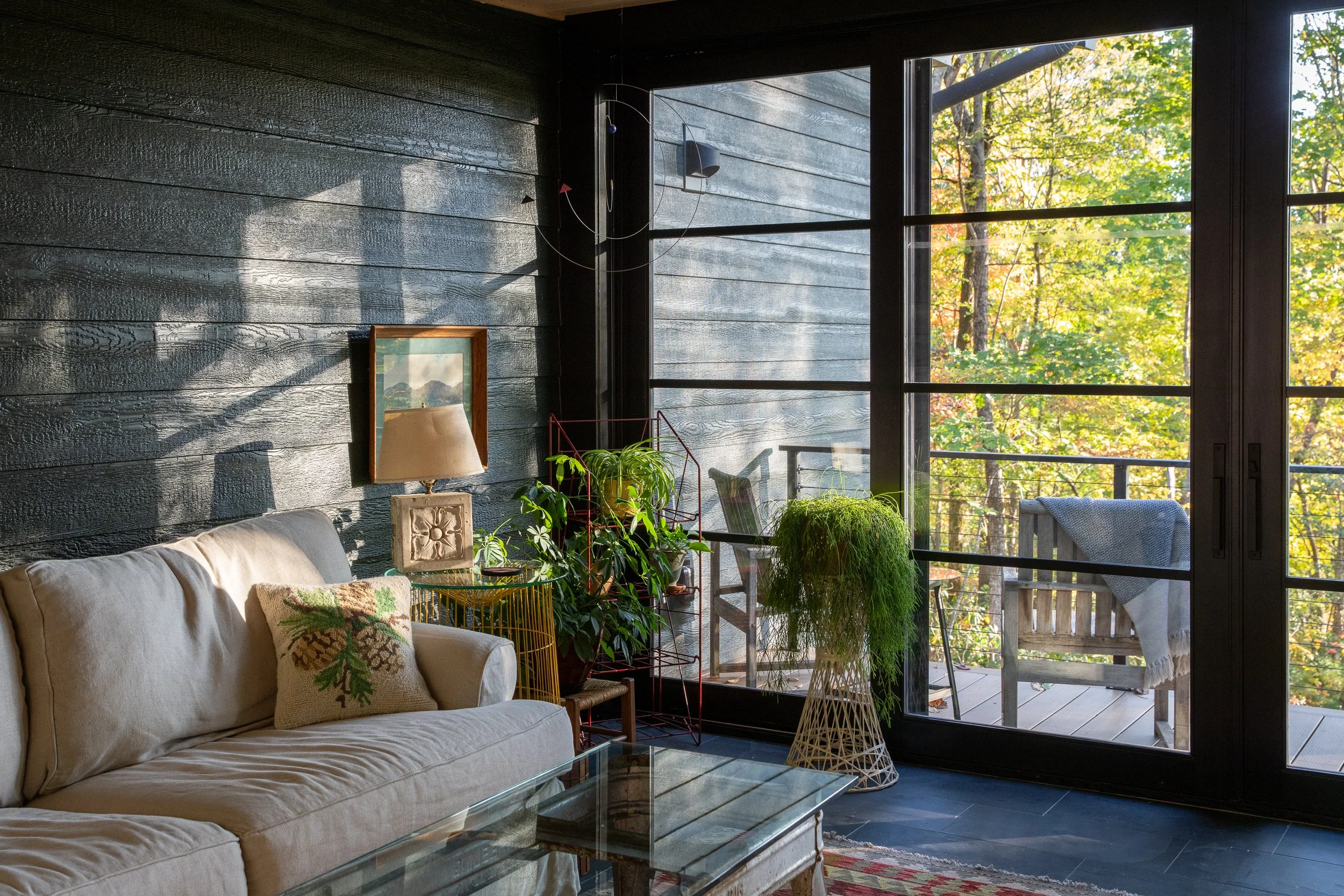 Small sitting room with black wood walls, plants, and sliding glass doors to the deck.