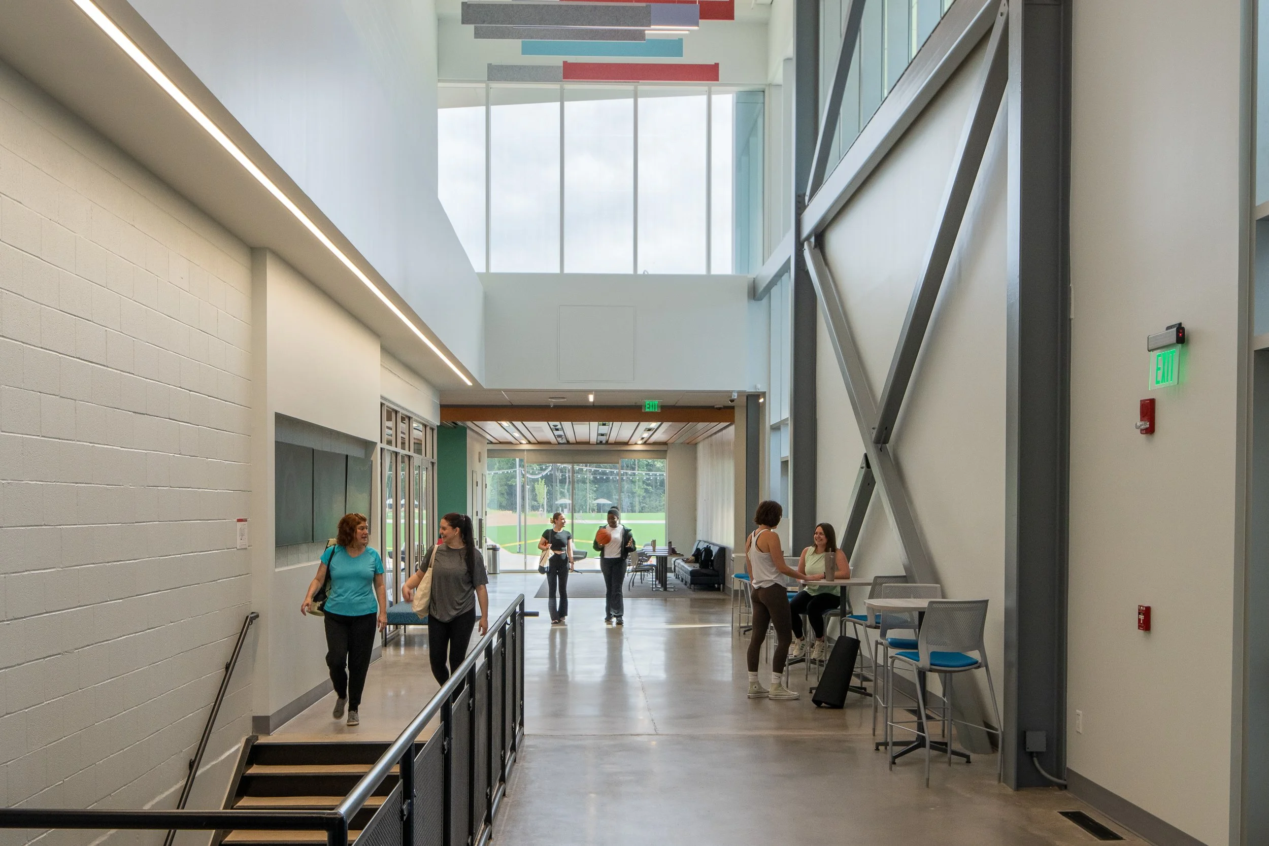 Double-height corridor with stairs, seating areas, exposed structural bracing and daylight from clerestory windows.