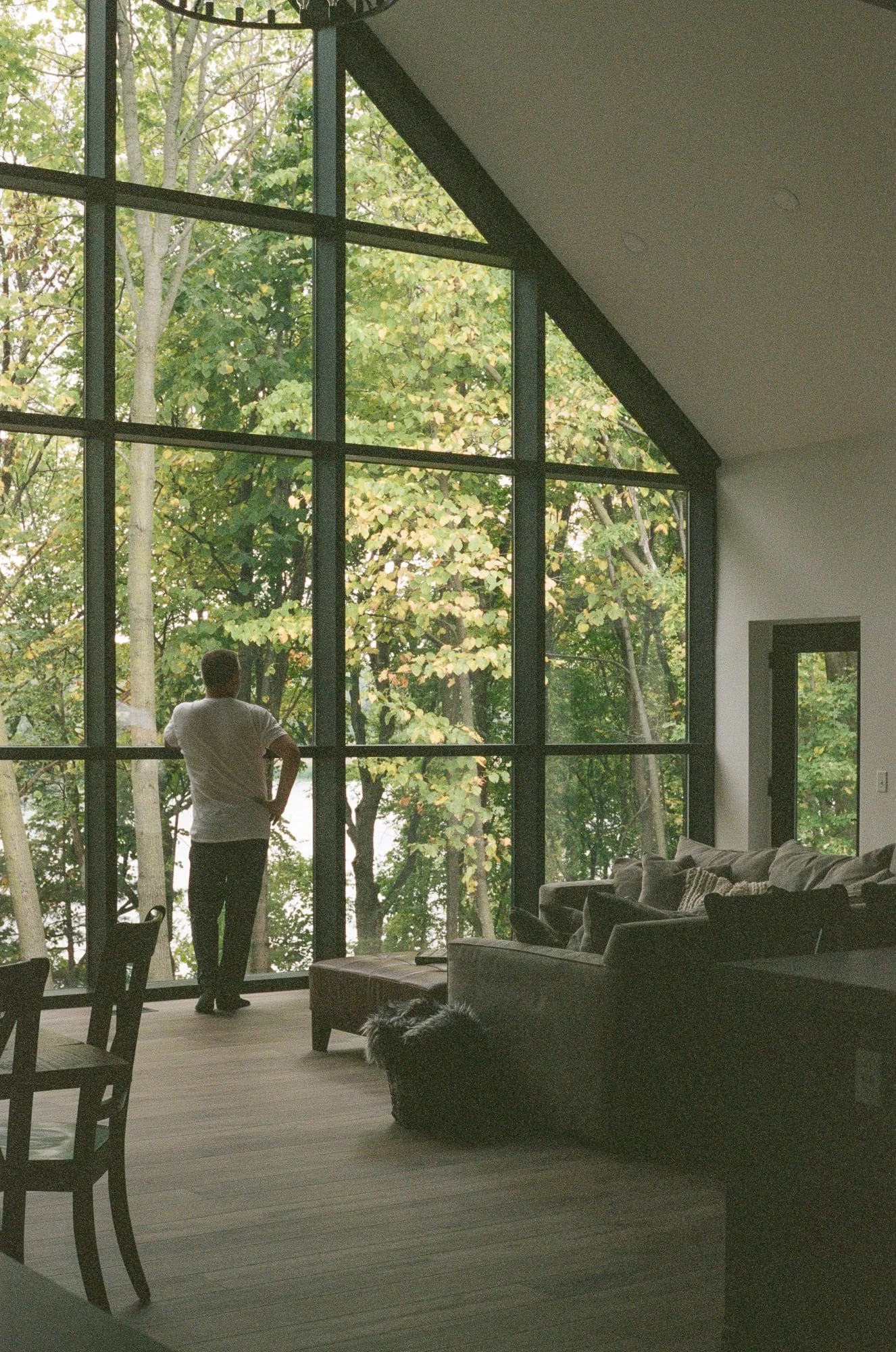 Gabled living room with floor-to-ceiling glass and a figure in the frame, one of the strongest images from the film experiment