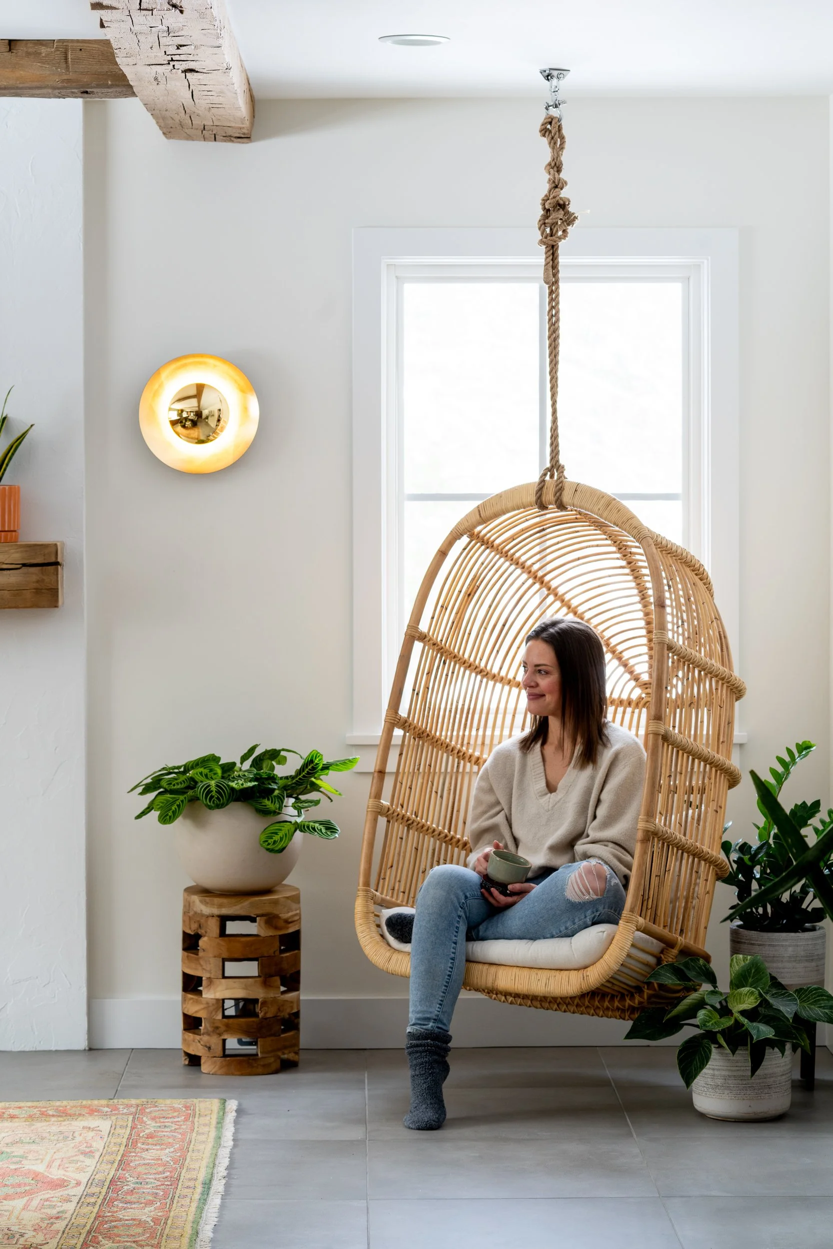 A cozy living space with a rattan hanging chair, natural light, and plants.