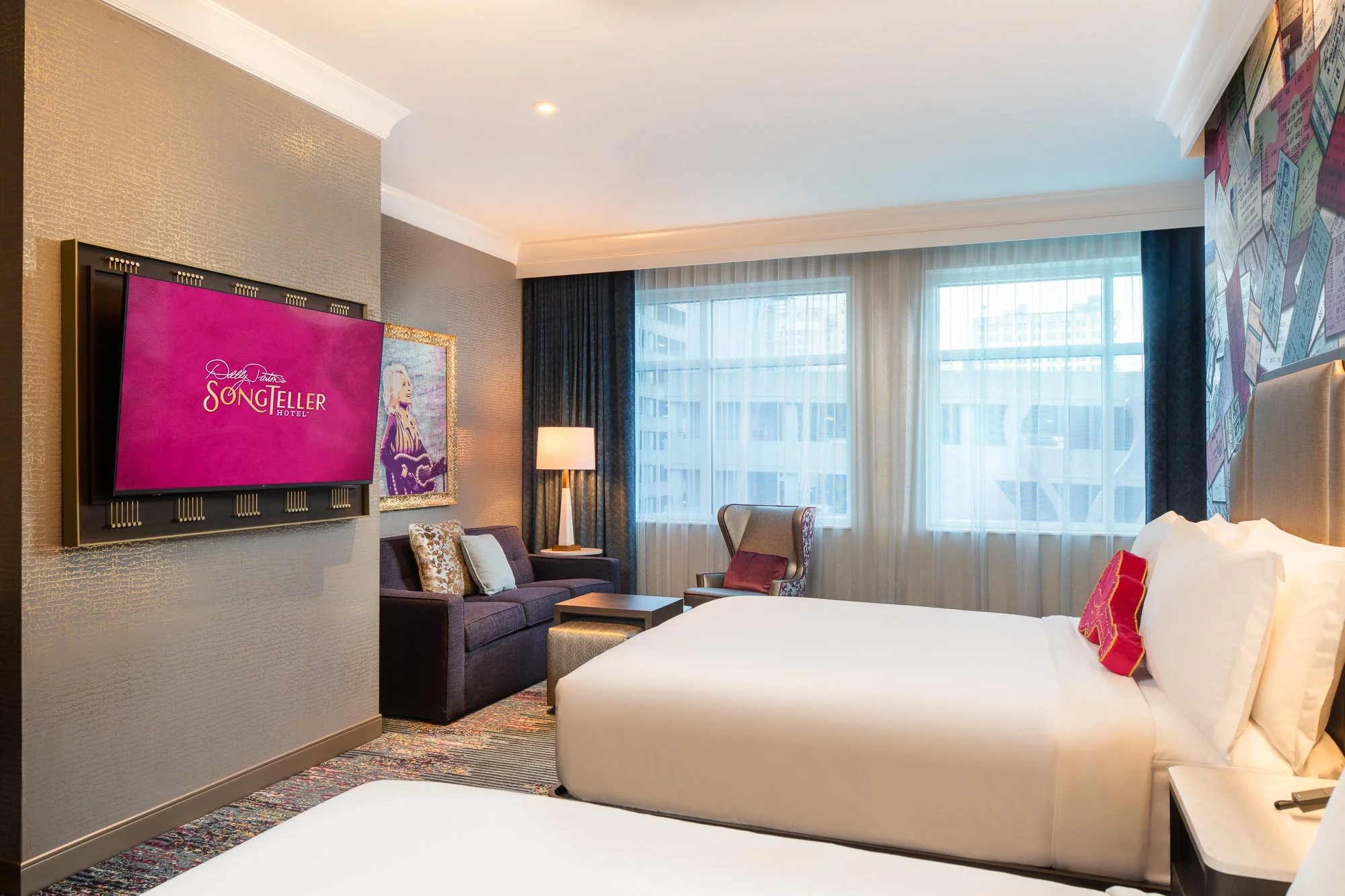 Double queen guest room at SongTeller Hotel with white bedding, framed artwork, blue drapery, and a colorful concert-ticket mural.
