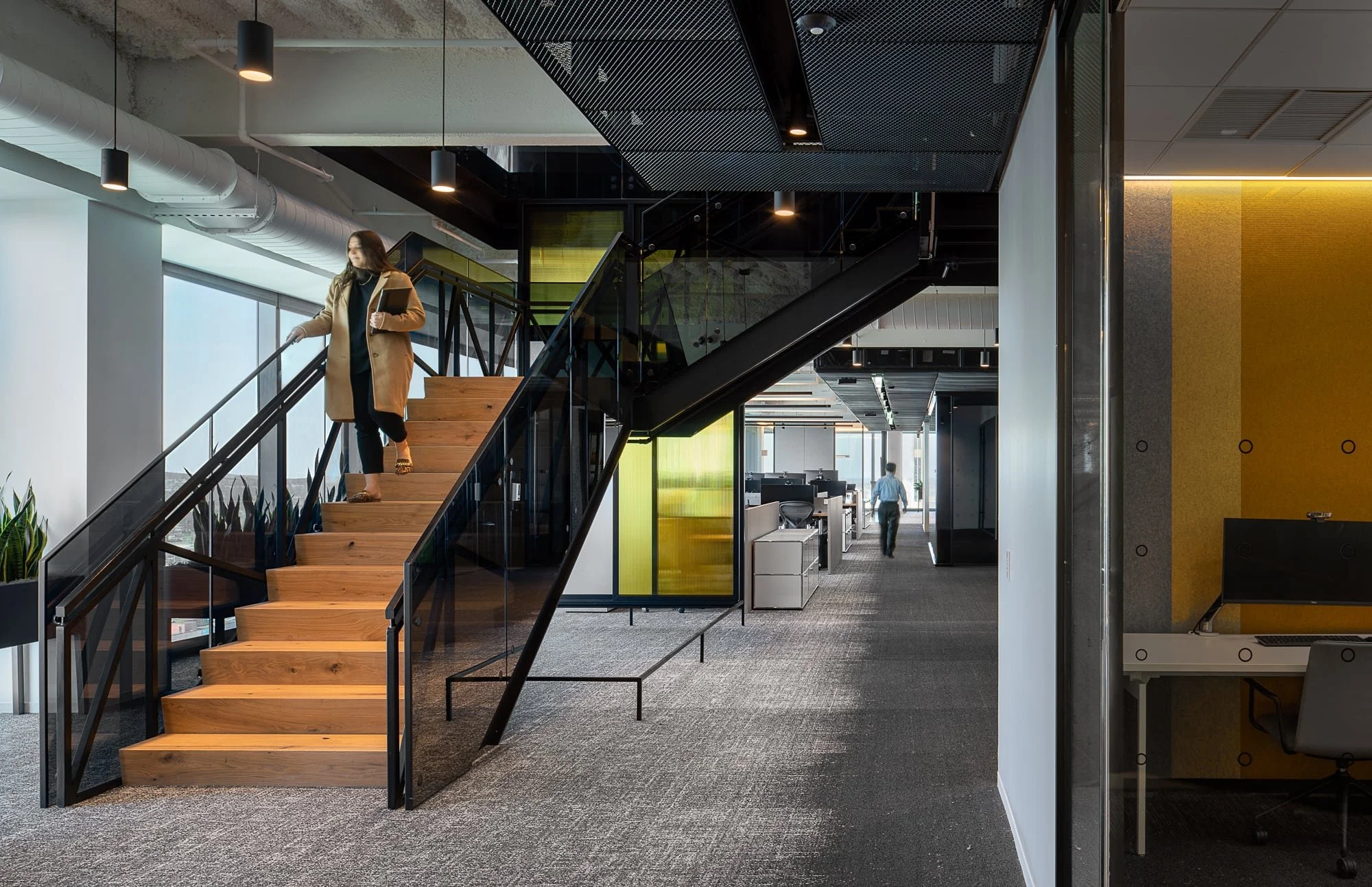 Alliance Bernstein Nashville interior stair with wood treads, black steel railings, yellow glass accent panels, and an employee descending toward the open office floor