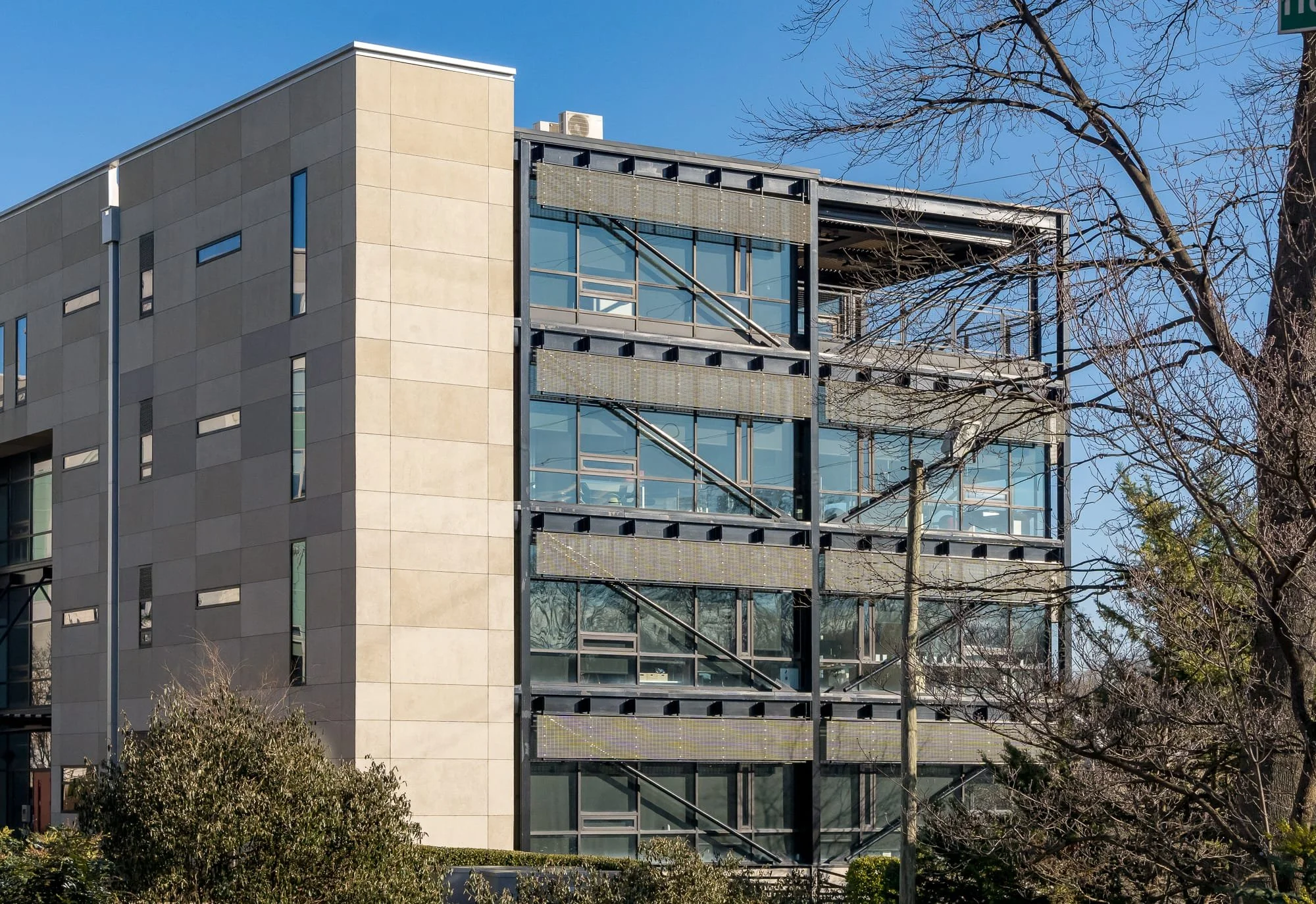 Modern multistory building with exposed steel framing, large windows, and bare tree branches in downtown Charlotte.