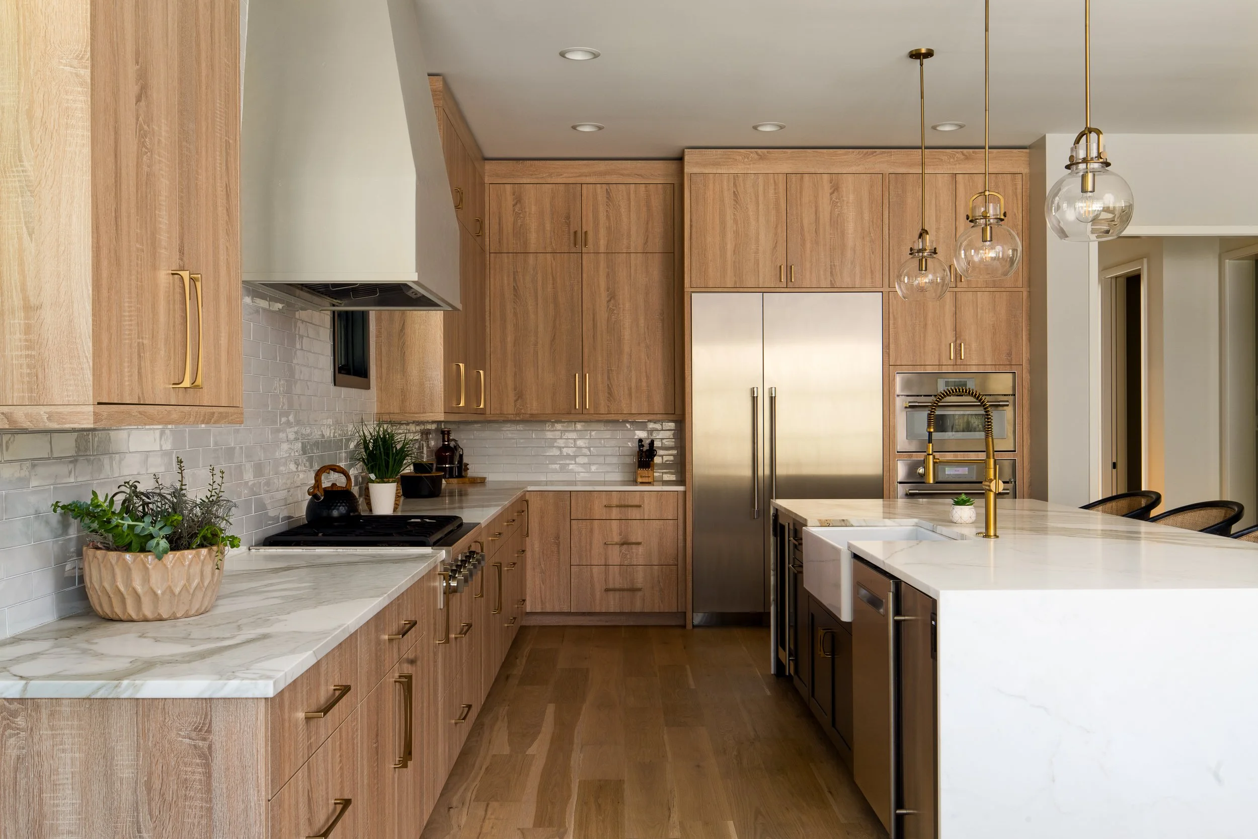 Modern kitchen with wooden cabinets, white marble countertops, a stainless steel refrigerator, and pendant lights with glass globes hanging from the ceiling.