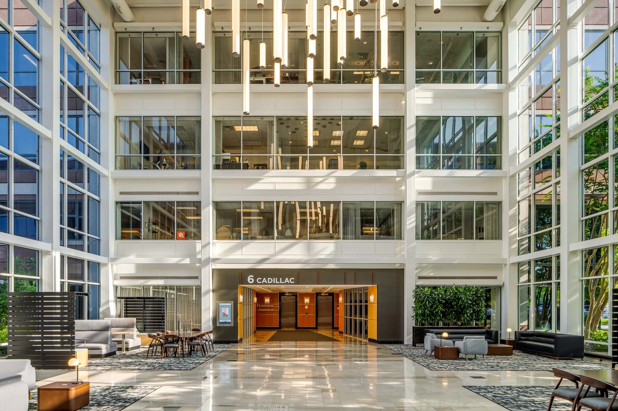 Multi-story office atrium with glass walls, indoor courtyard seating, and suspended linear lighting.
