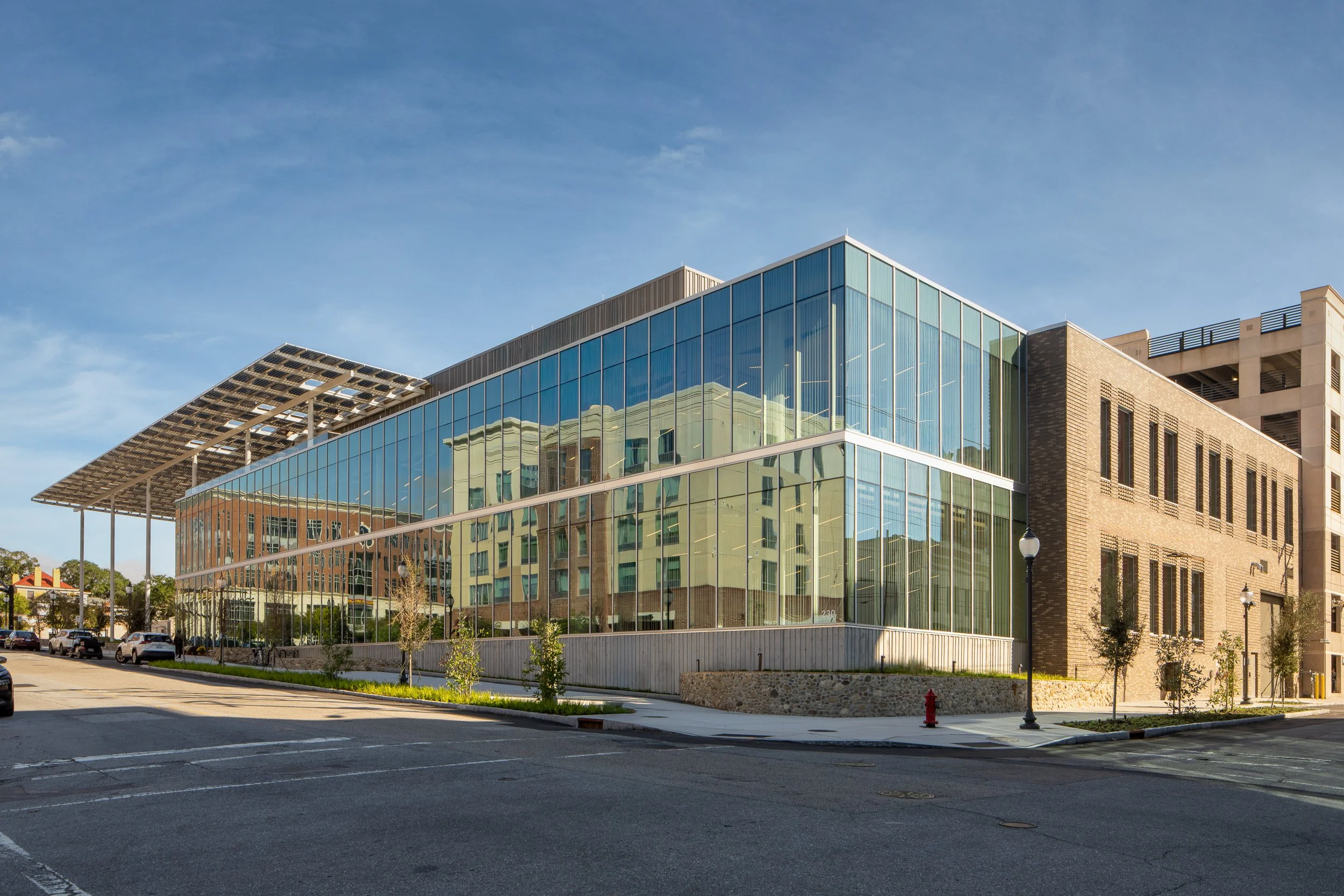 Daytime exterior of New Hanover County Library and Cape Fear Museum with glass curtain wall, brick volume, and solar canopy.