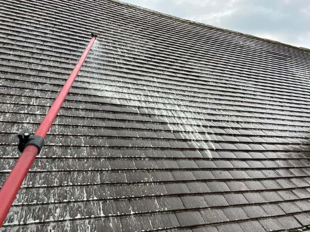 A power washer cleaning a brown tiled roof, spraying water from a red wand.