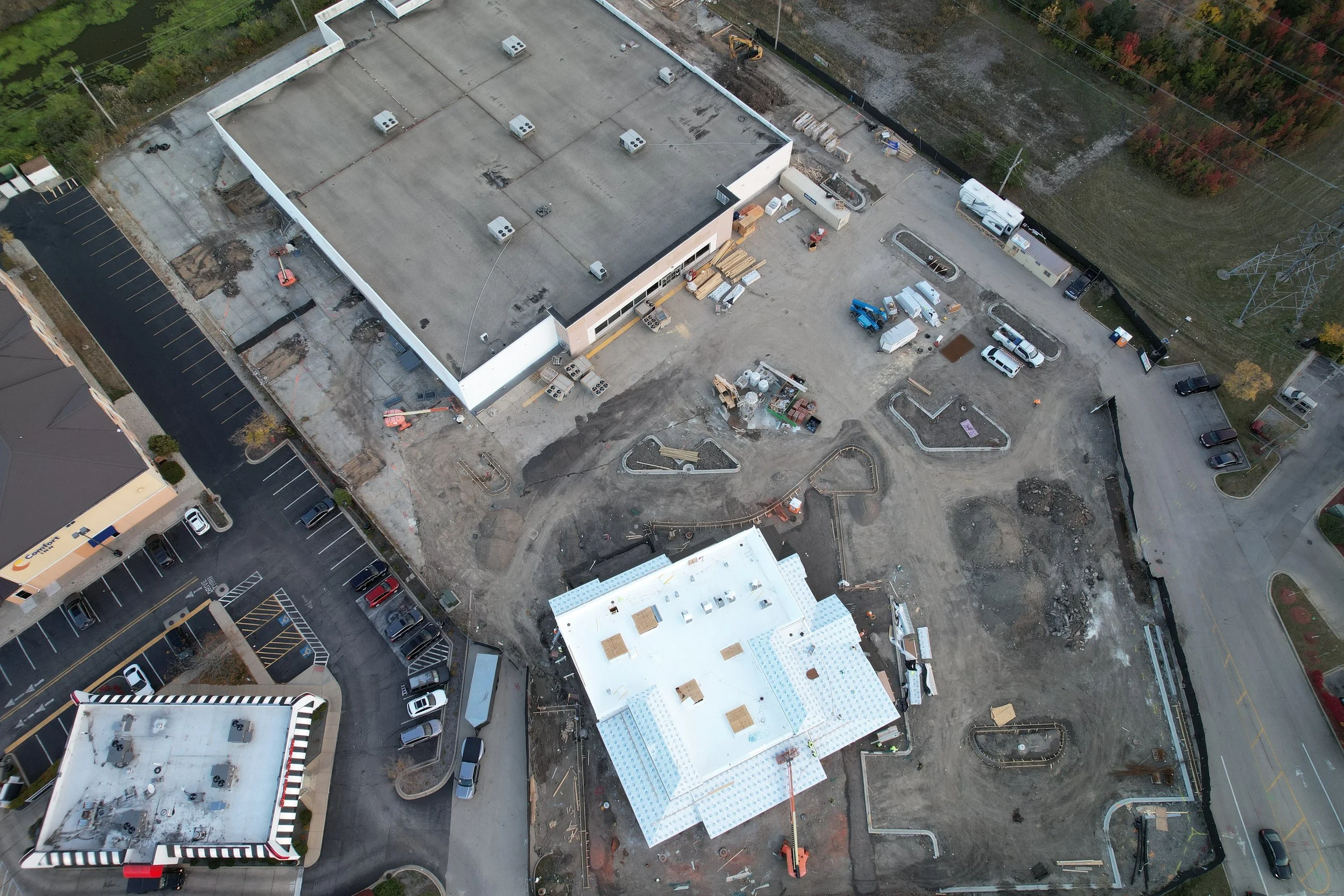 Aerial view of a construction site with partially built structures, construction equipment, and parked vehicles.