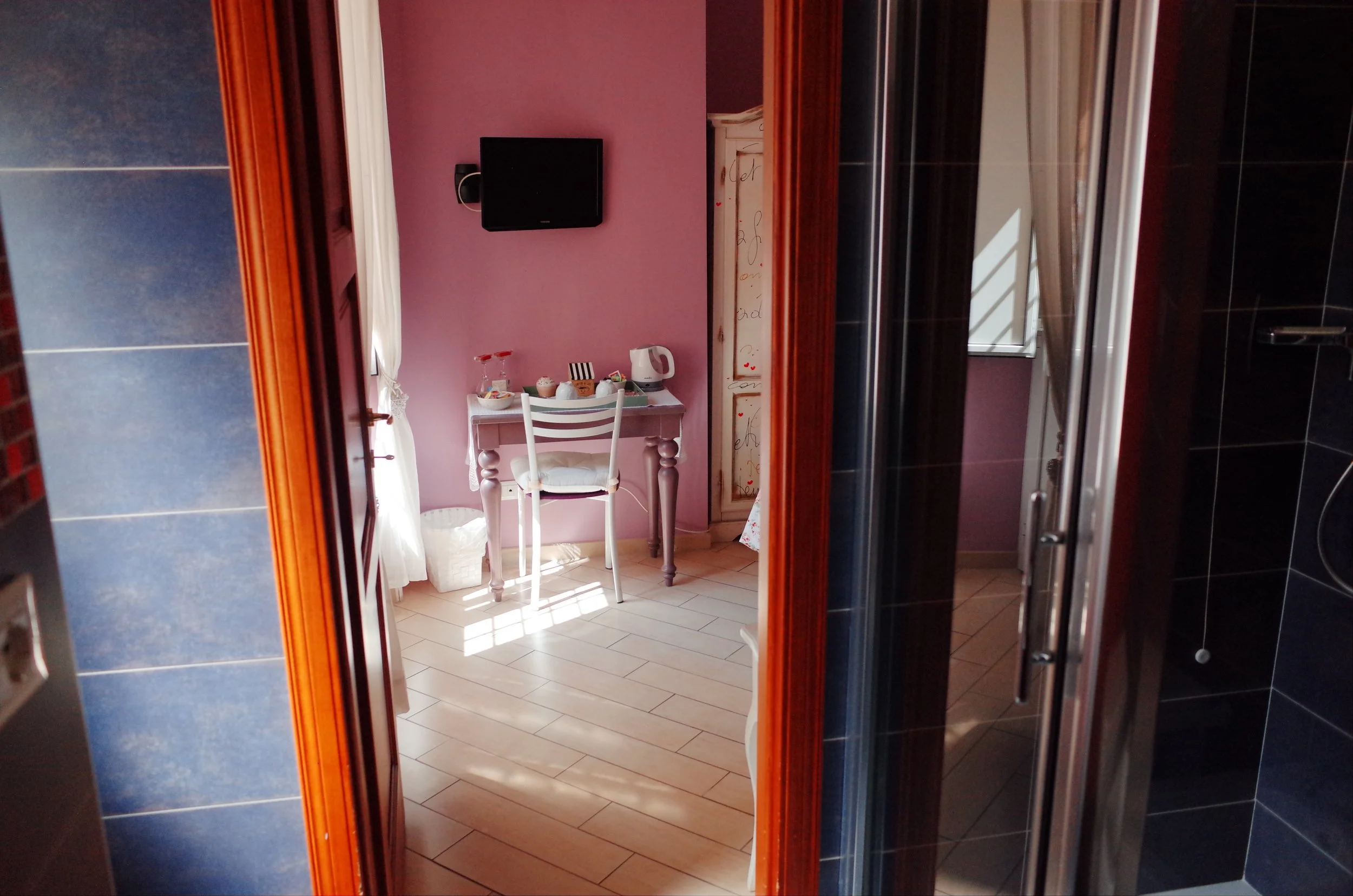 View through a doorway into a room with lavender walls, a small white table with a chair, and a television mounted on the wall.