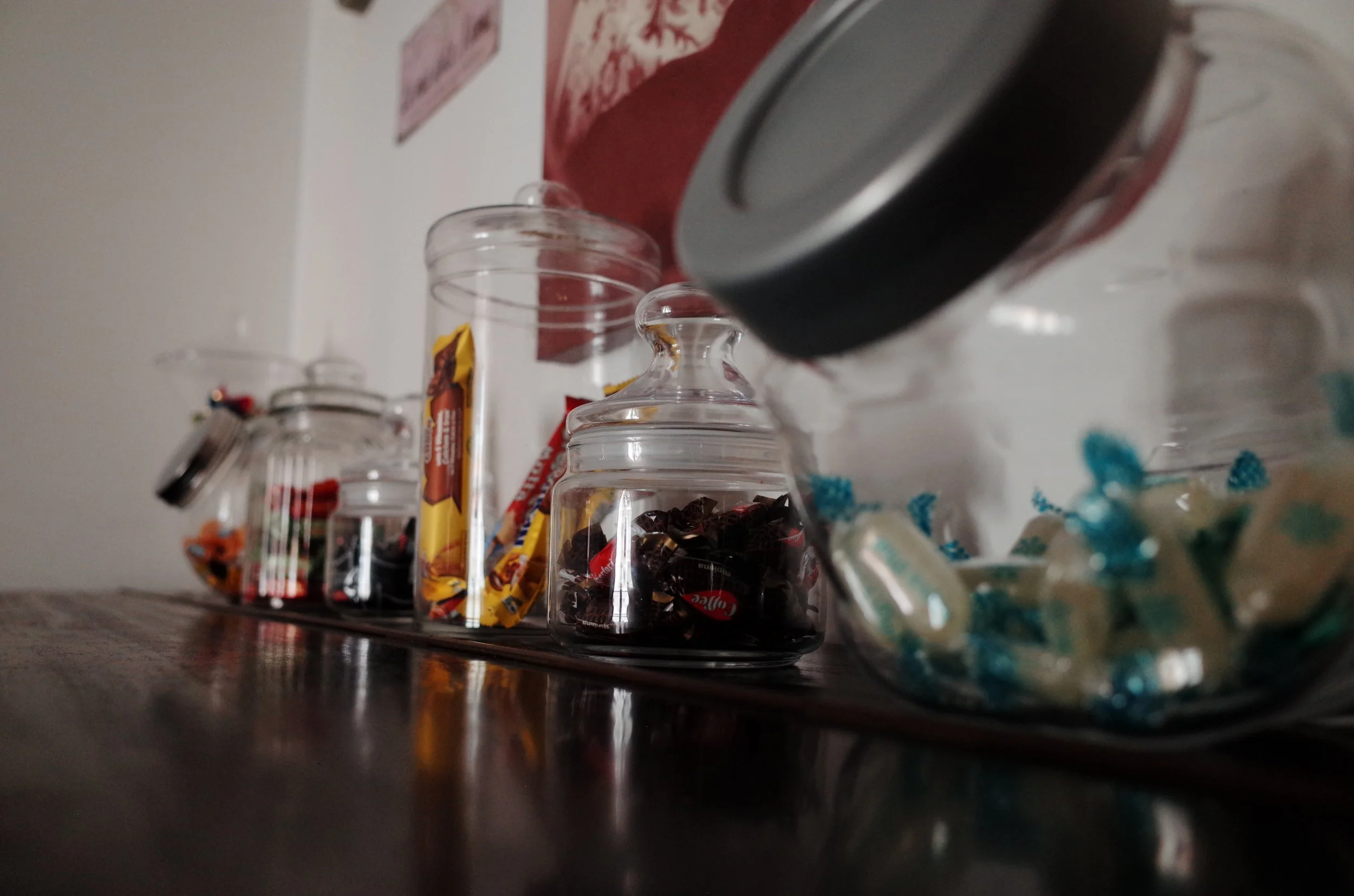 A collection of glass jars and containers filled with candy and snacks on a dark wooden surface.