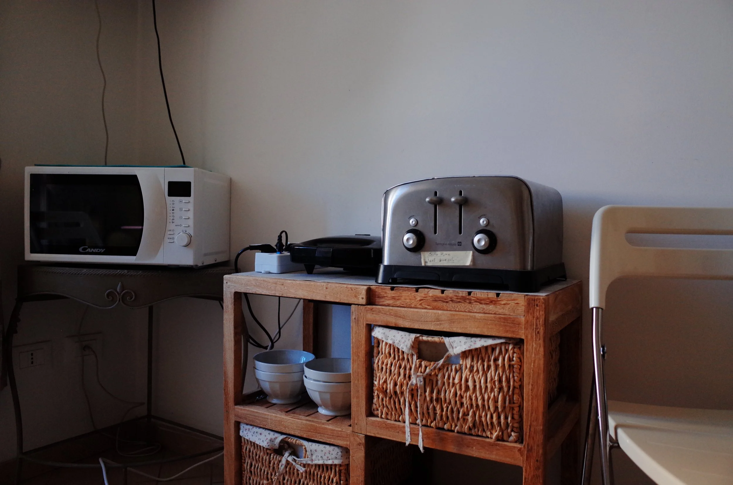 Kitchen area with a microwave oven, a toaster, and a small wooden table with baskets and bowls underneath.
