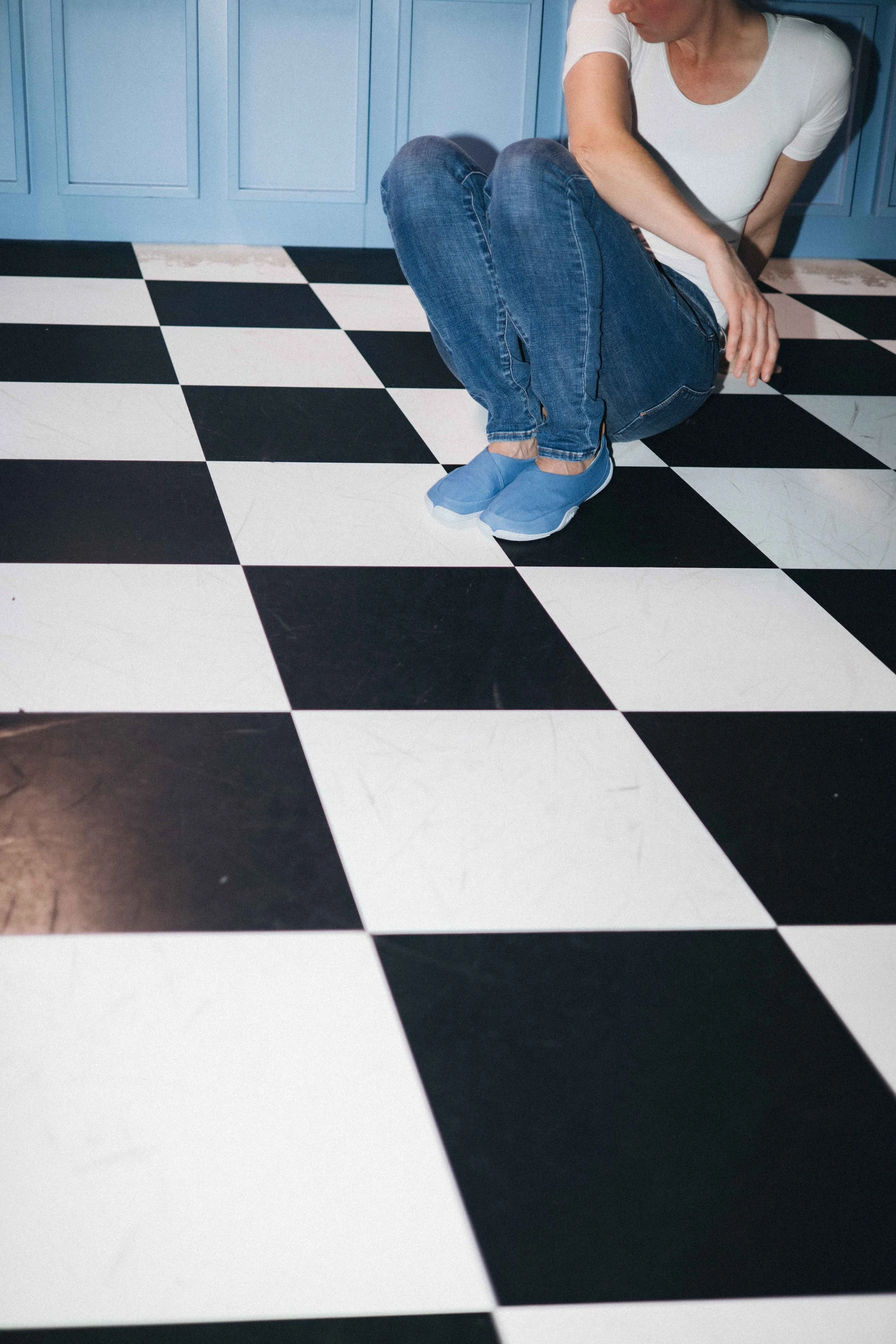 High Fashion Fotoshooting in München. Frau mit Jeans sitzt auf kariertem Fußboden. Es wurde hart geblitzt.