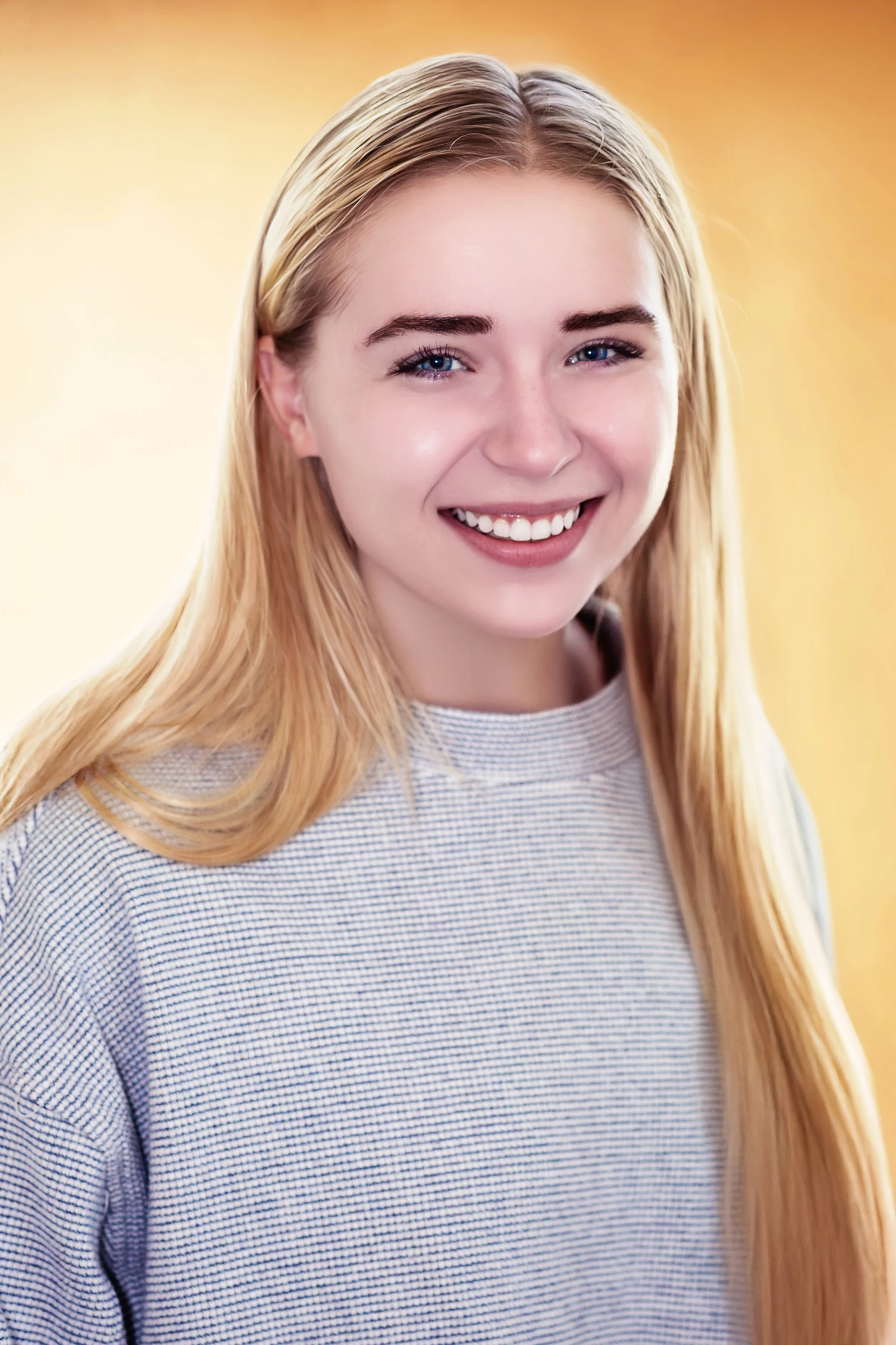 A young woman with long blonde hair smiling against a yellow background. Headshot Photography in Loveland, Colorado. Jeanette Fellows Photography www.fellows.photos