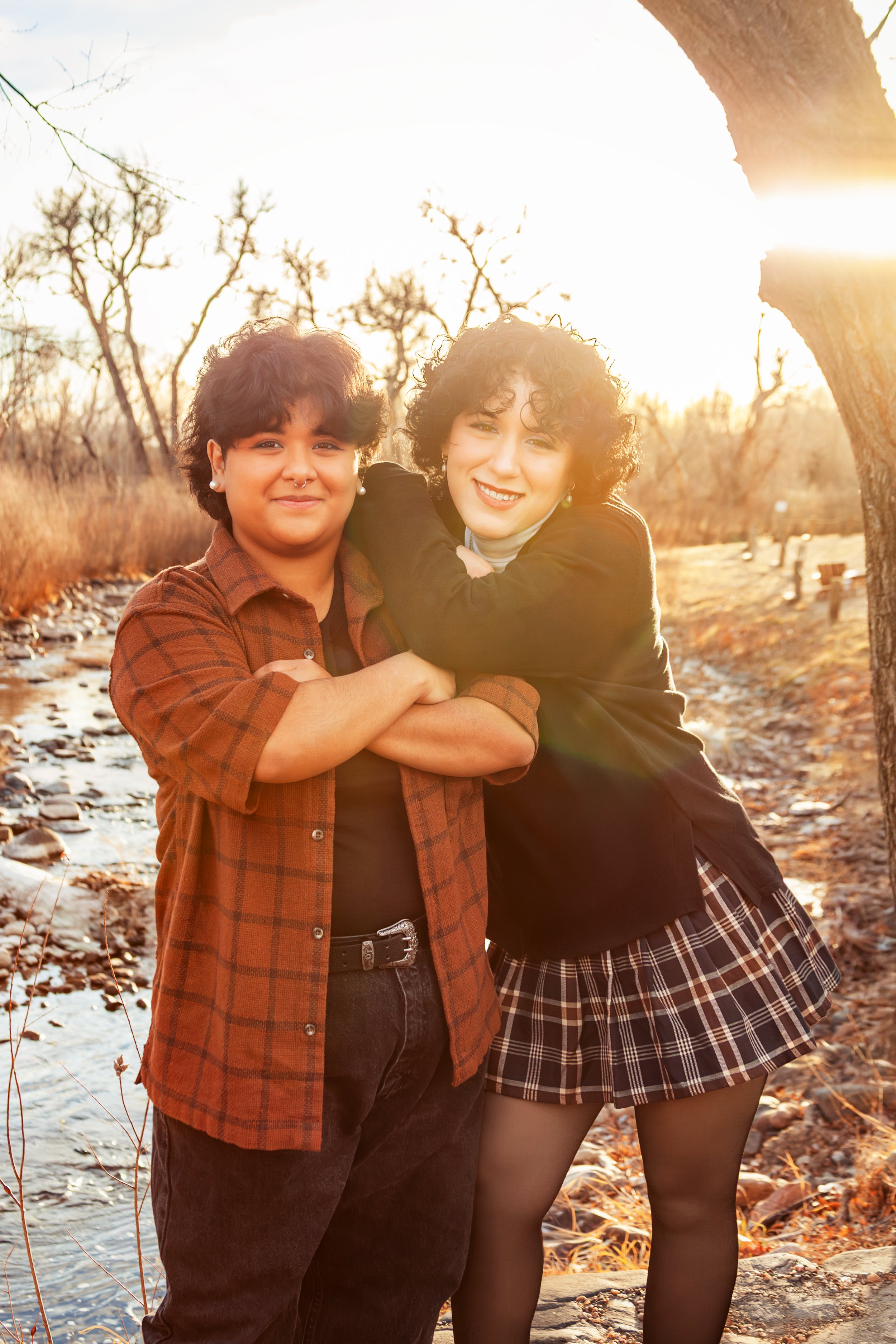 Two women standing outdoors in a creekside setting during sunset, smiling, with one embracing the other. Jeanette Fellows Photography www.fellows.photos