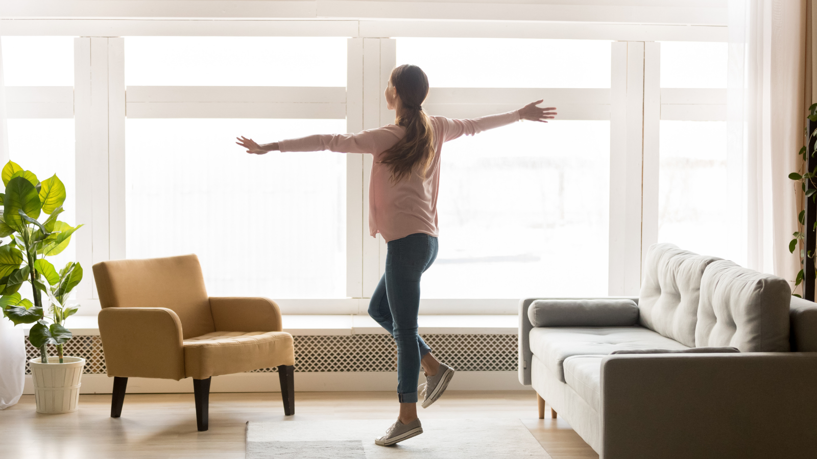 Woman standing in a bright, sunlit living room with arms spread wide, embracing a fresh start and new beginning after divorce.