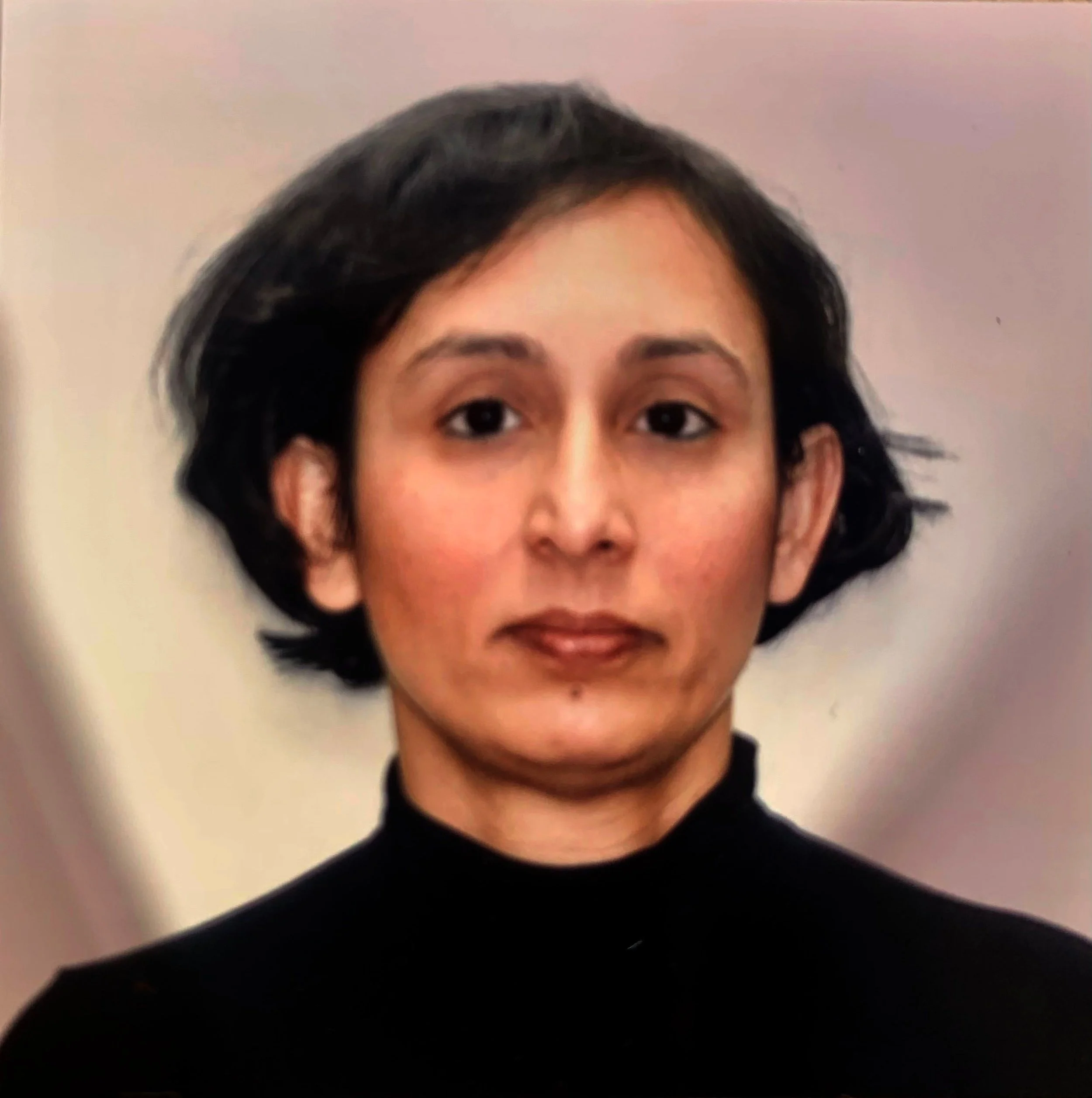 Woman with dark brown hair working at a craft table, wearing a striped shirt, surrounded by art supplies and a pegboard with tools in a craft room.
