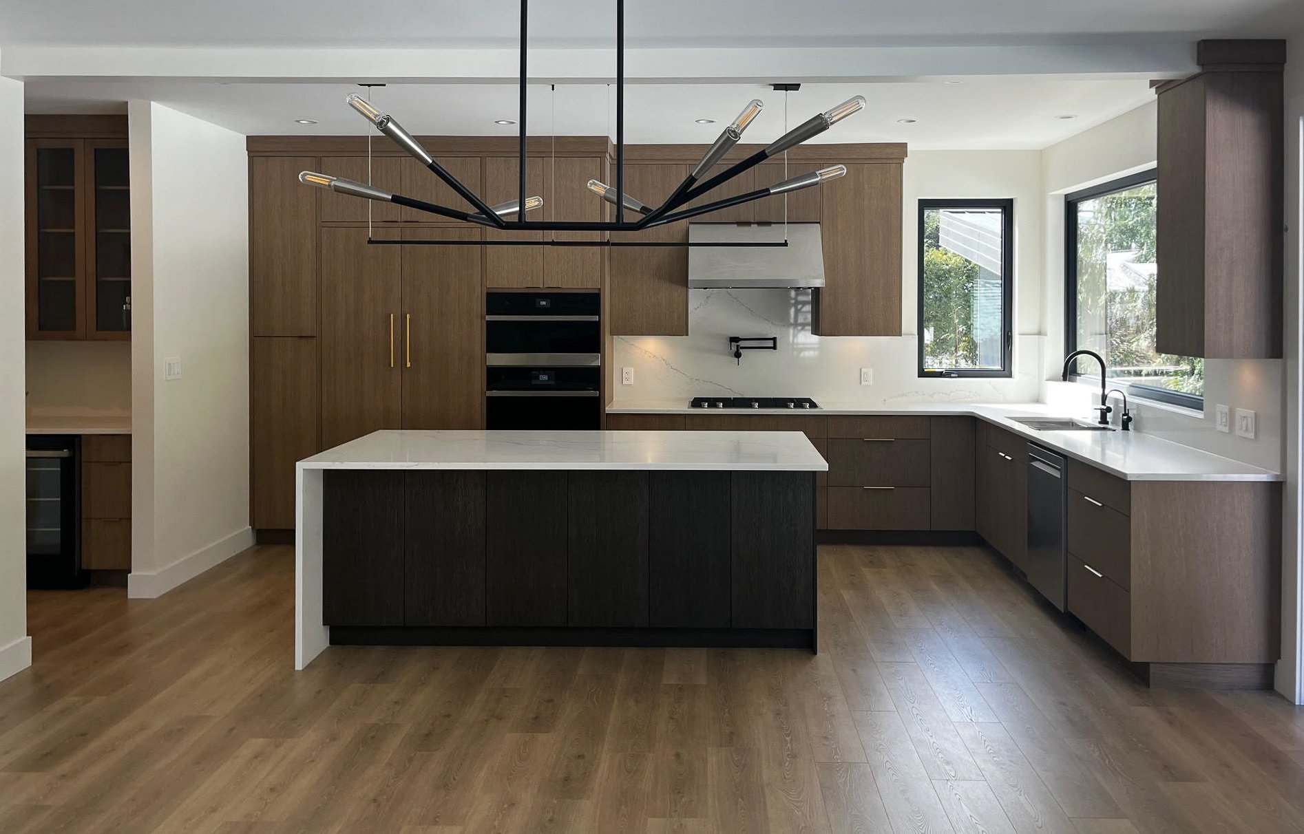 Modern kitchen with a central island, dark wood cabinetry, light countertops, built-in appliances, and a contemporary chandelier.