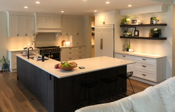 Modern kitchen with large island, bar stools, white cabinets, floating shelves, and stainless steel appliances.