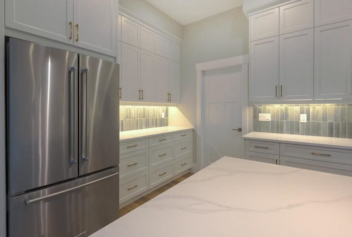Modern kitchen with stainless steel French door refrigerator, white cabinets, and marble countertops.