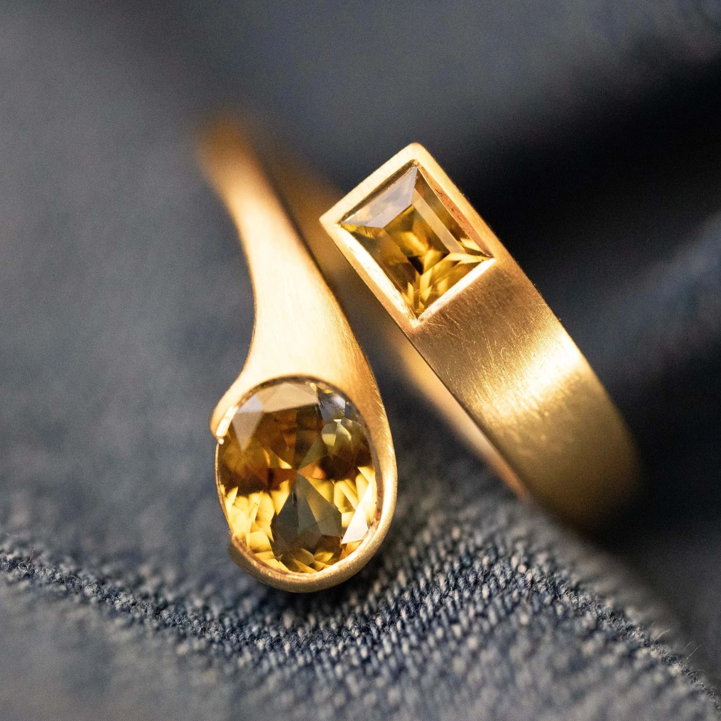 An 18k yellow gold ring with two yellow/teal bicolor sapphires on a blue fabric background