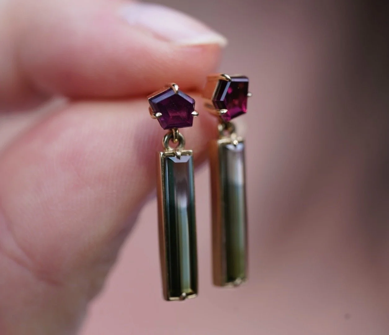 maroon freeform garnets and blue/green bicolor tourmaline dangle earrings held by a hand