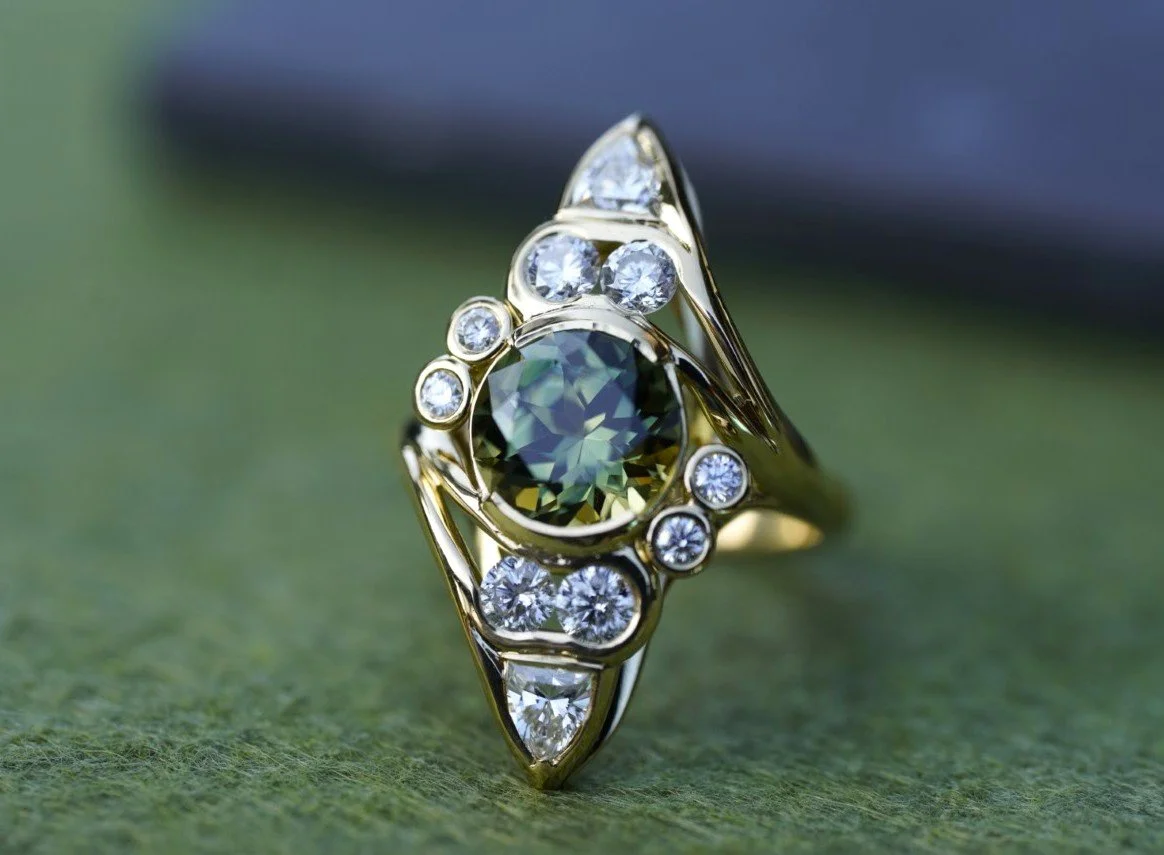 A gold ring featuring an oval-shaped dark green gemstone surrounded by multiple small clear diamonds.